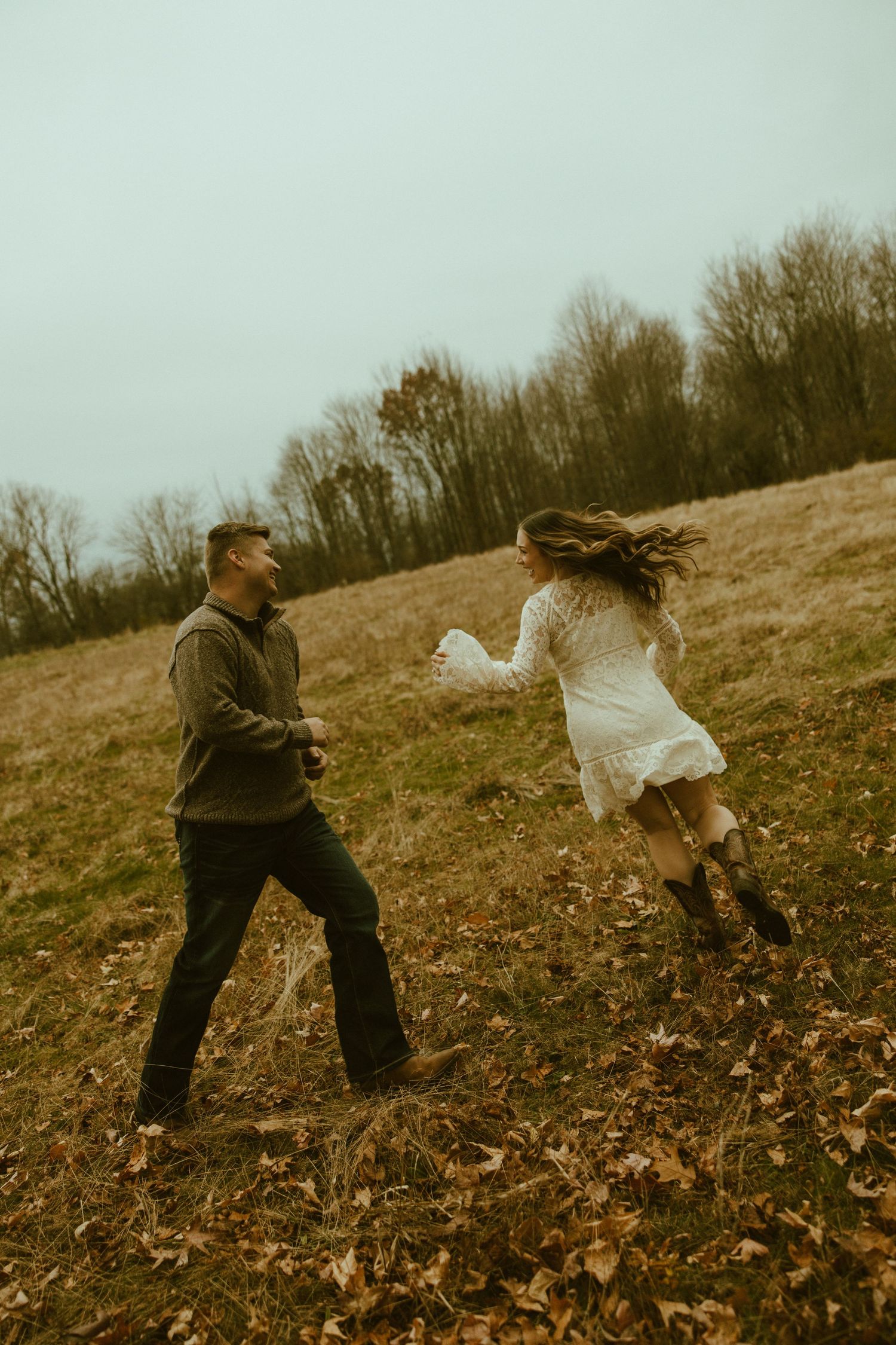 Two people playfully spinning and dancing together on a hillside covered in autumn leaves in muted vintage tones.