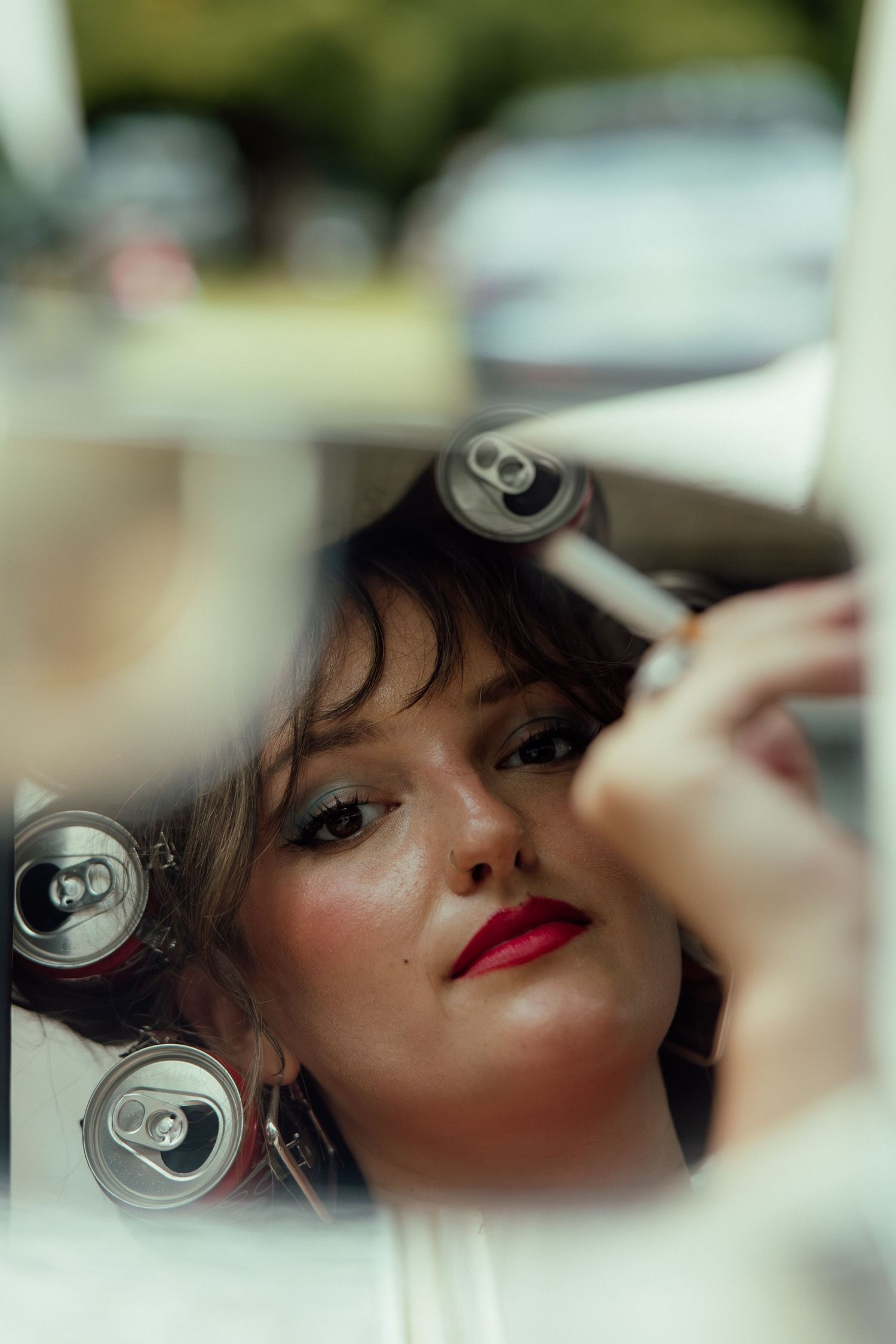 Artistic portrait reflected in mirror with soda cans, featuring red lipstick and soft lighting.