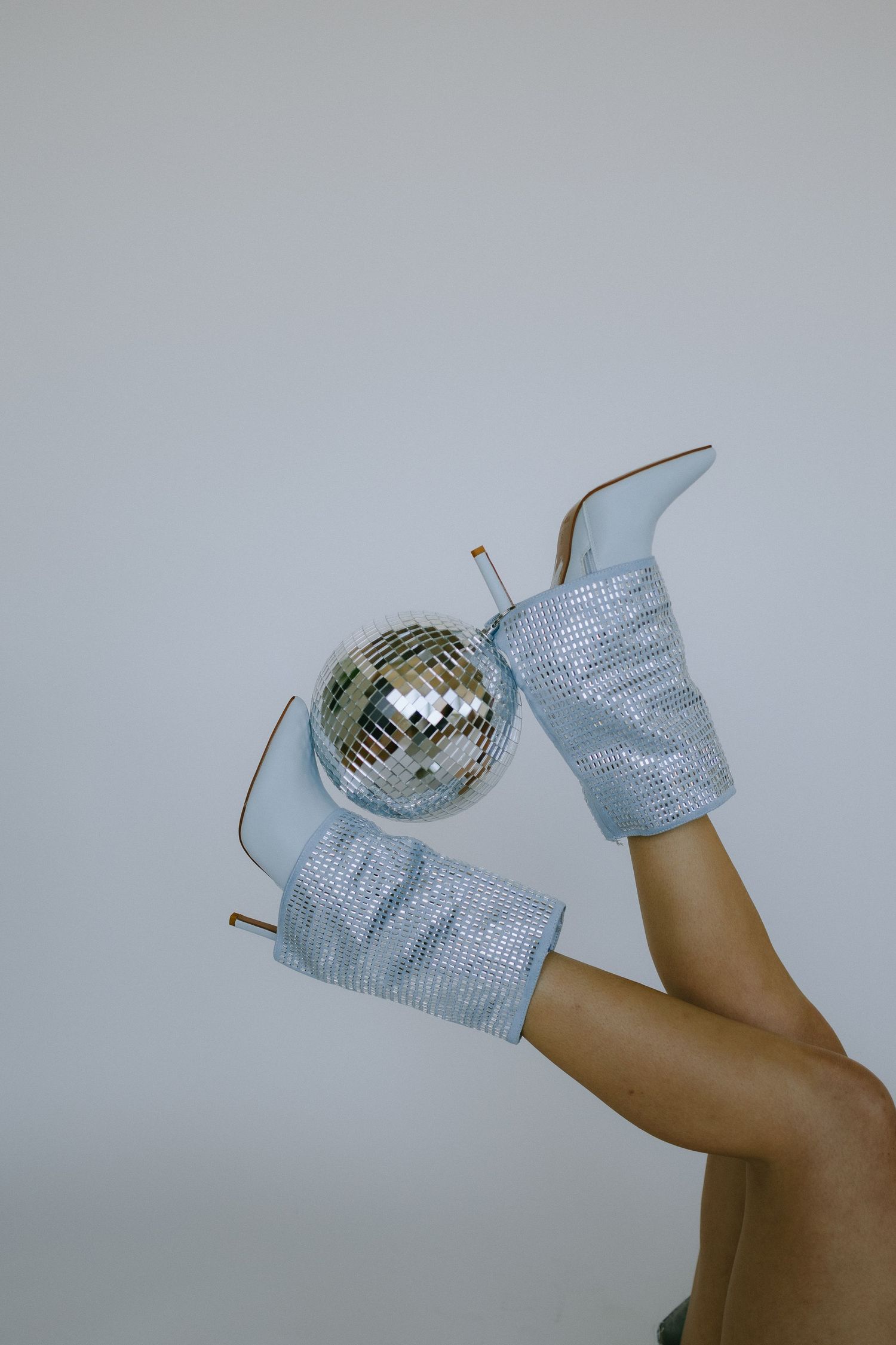 Sparkly silver boots and disco ball against grey background.