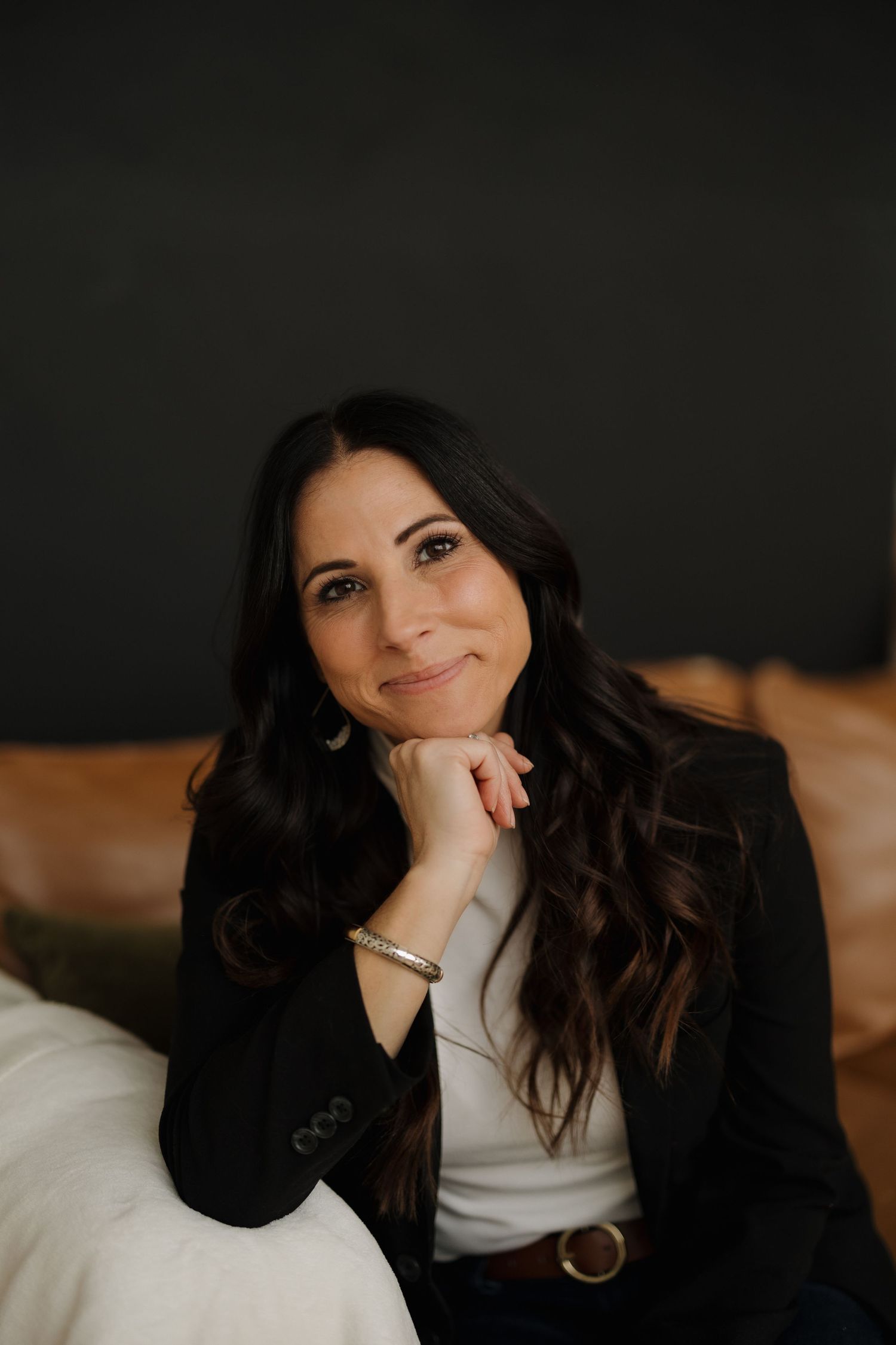 Professional headshot against dark background wearing black blazer and white top.
