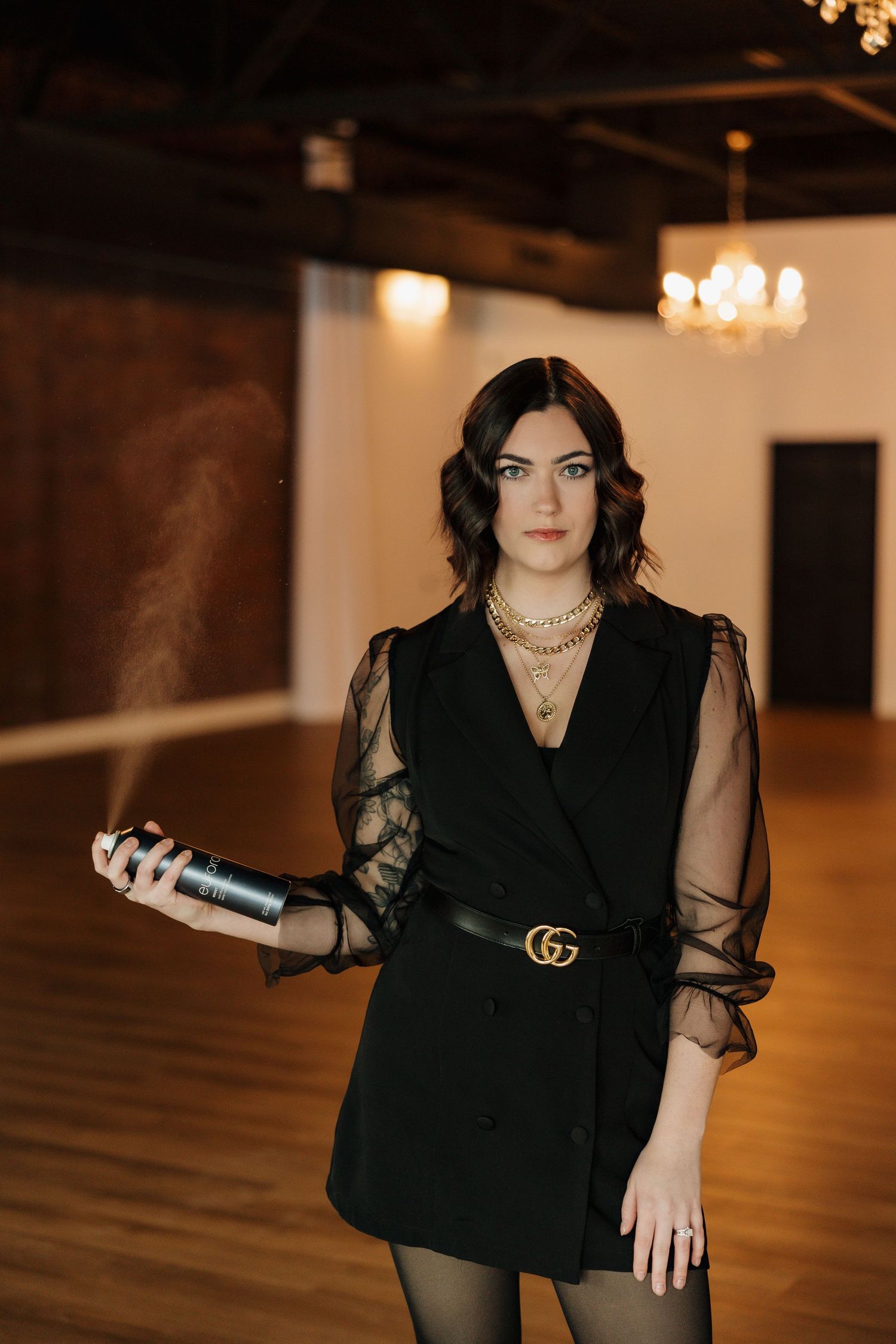 Elegant portrait in a black blazer dress with sheer sleeves holding a styling tool.