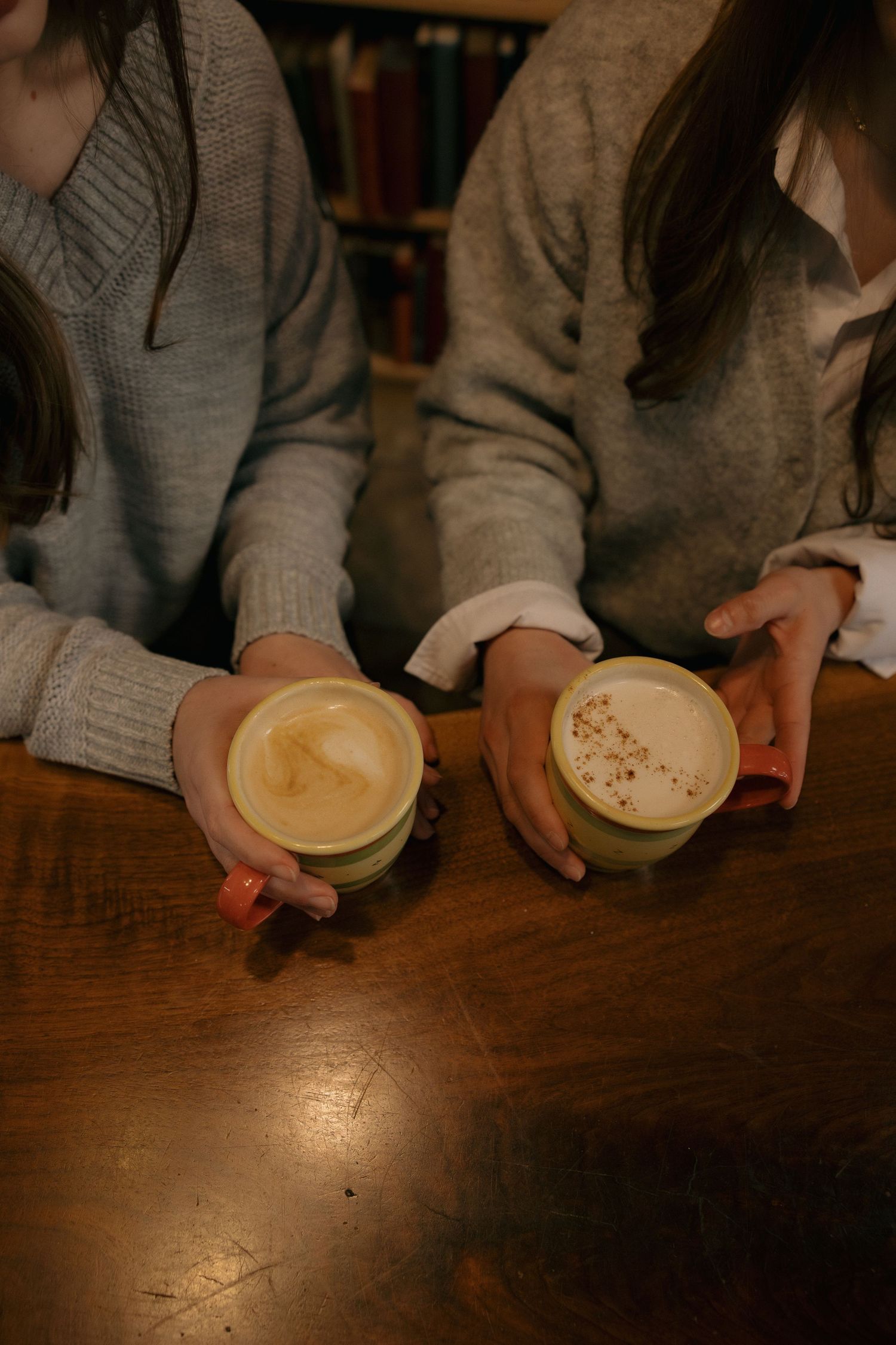 Two cups of latte with artistic foam designs on wooden table in cozy setting.