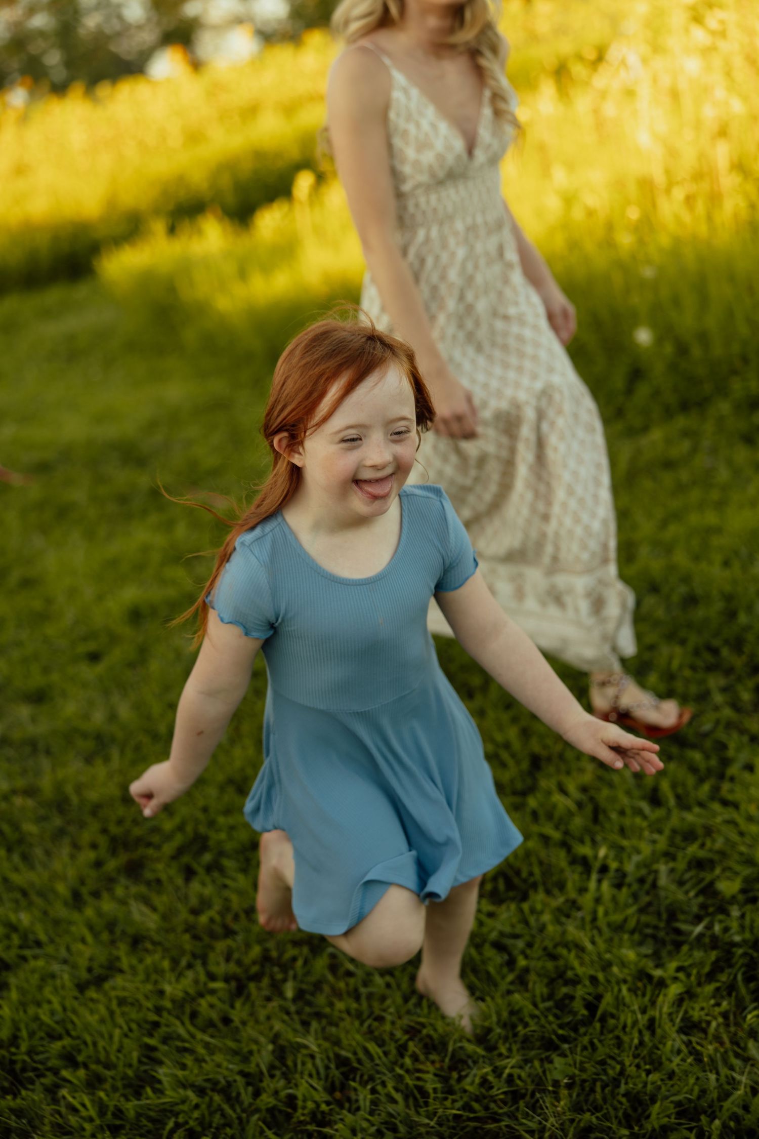 A joyful moment captured in a sunlit field with a blue dress and polka dot dress against golden evening light.
