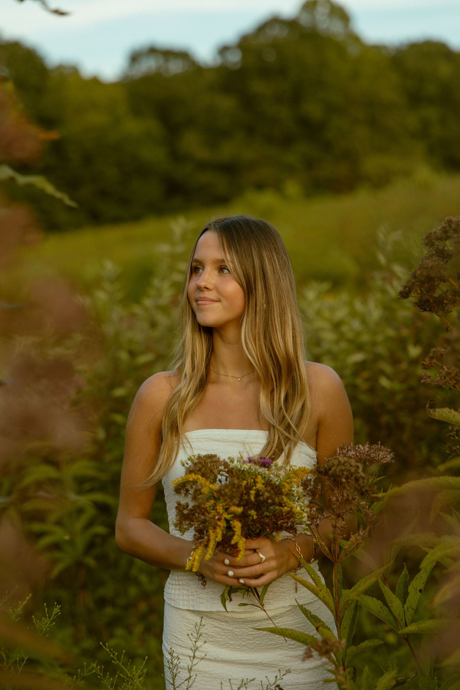 A dreamy outdoor photoshoot in a field with a white dress and wildflower bouquet at golden hour.