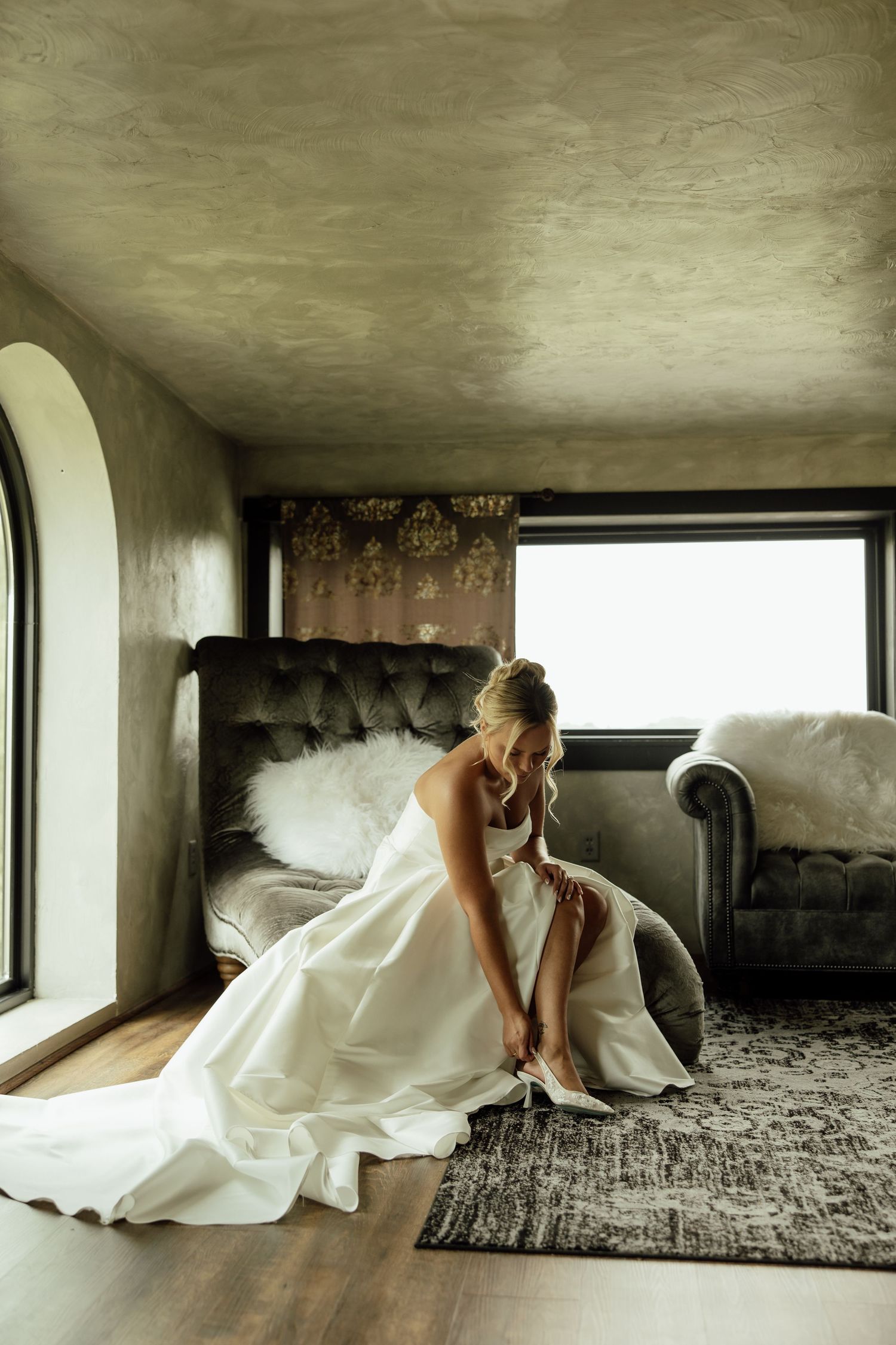 A figure in a flowing white dress crawls gracefully across a textured grey carpet in a minimalist interior space.