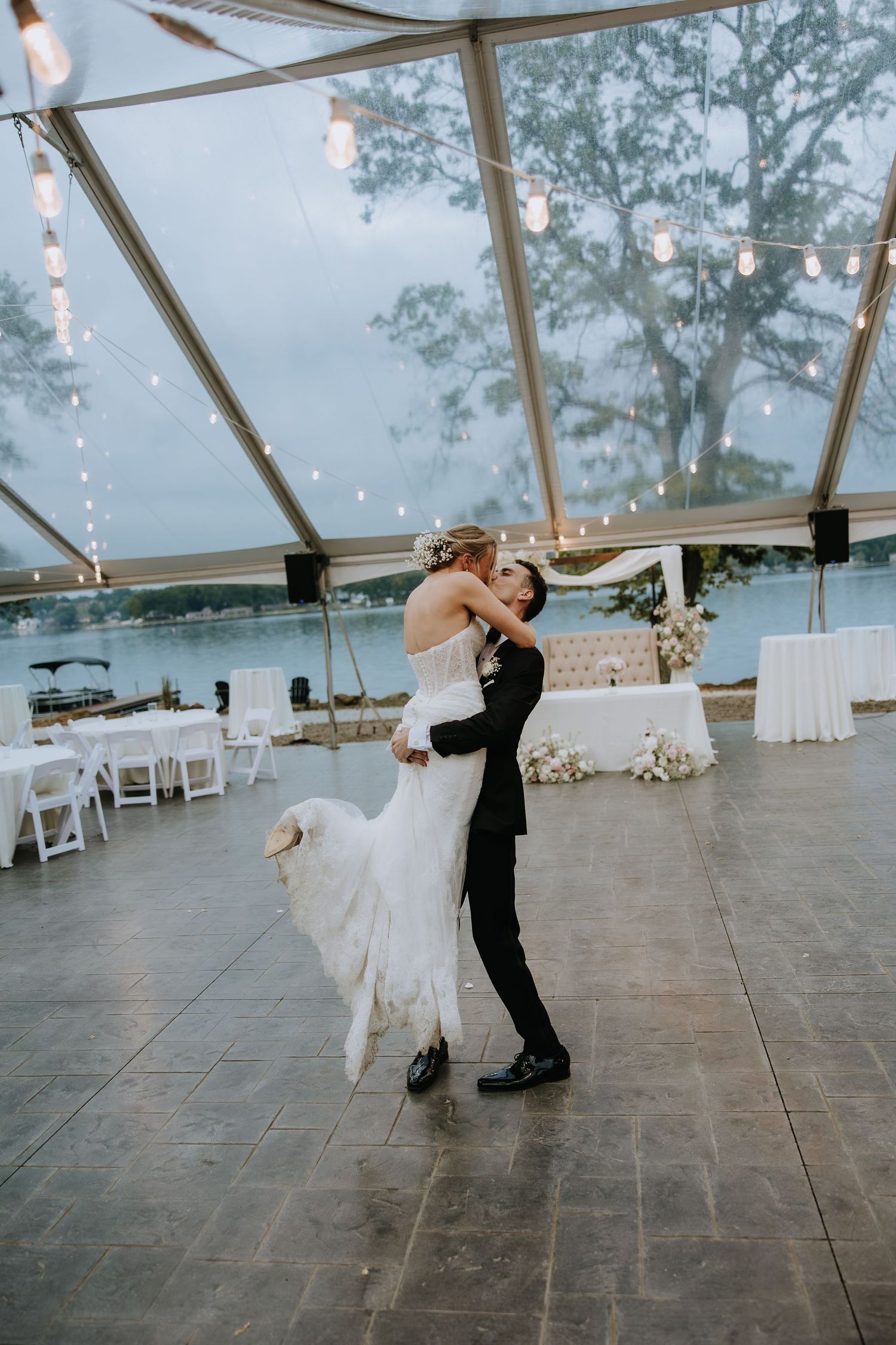 Couple's first dance in glass-ceiling venue with string lights and water view.