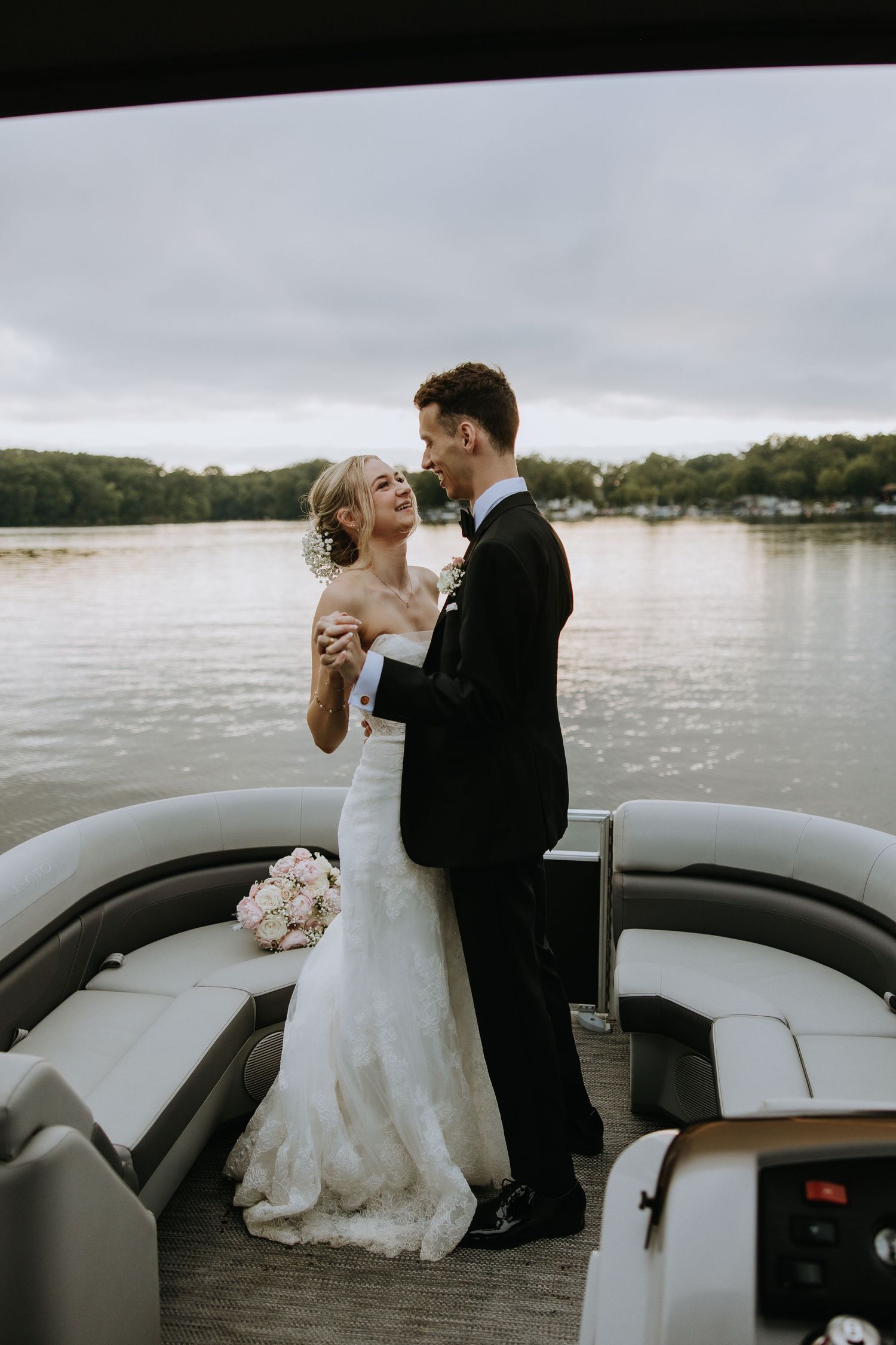 A romantic wedding couple embraces on a boat deck overlooking a serene lake.