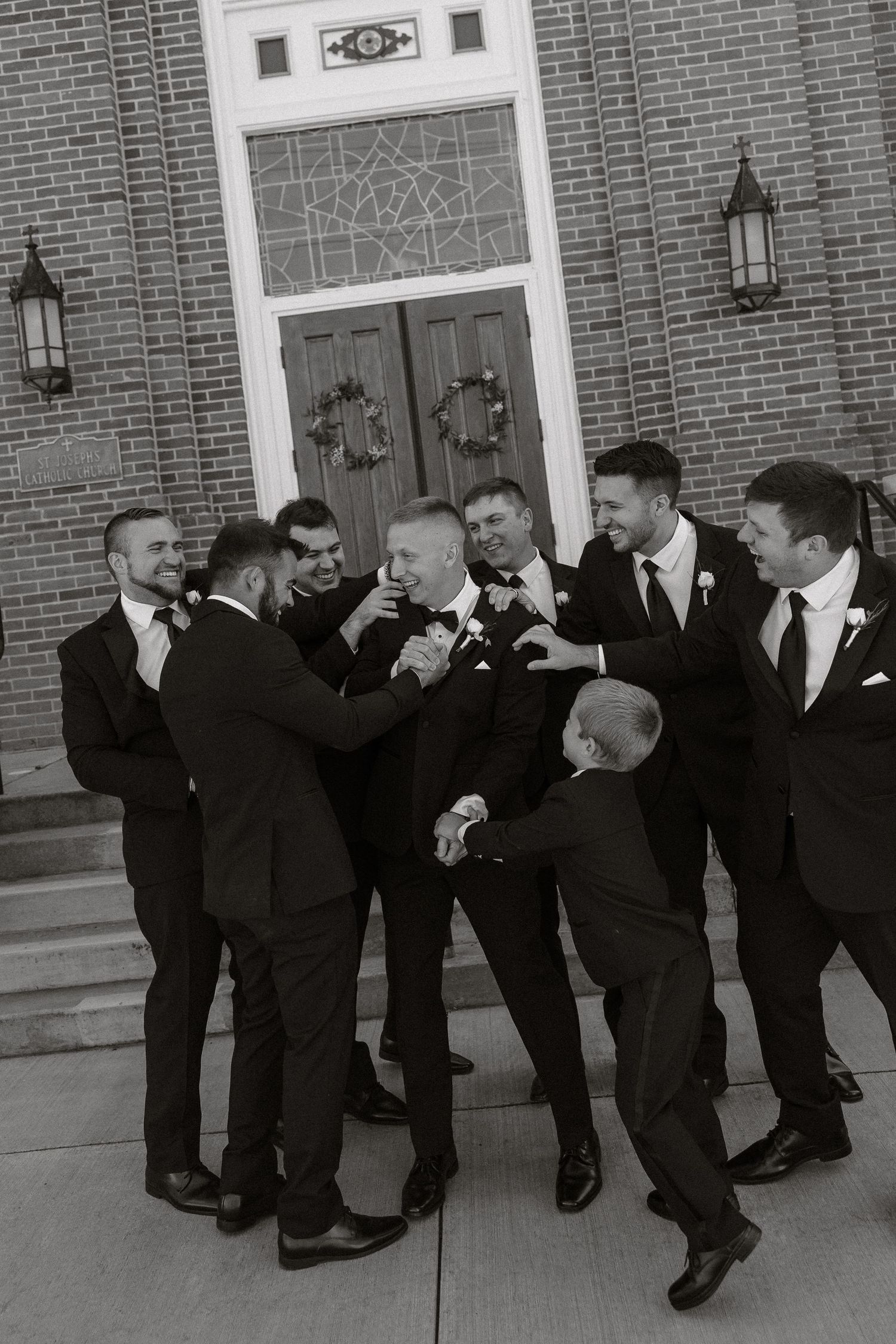 Black and white photo series of groomsmen in suits posing playfully outside a brick building.
