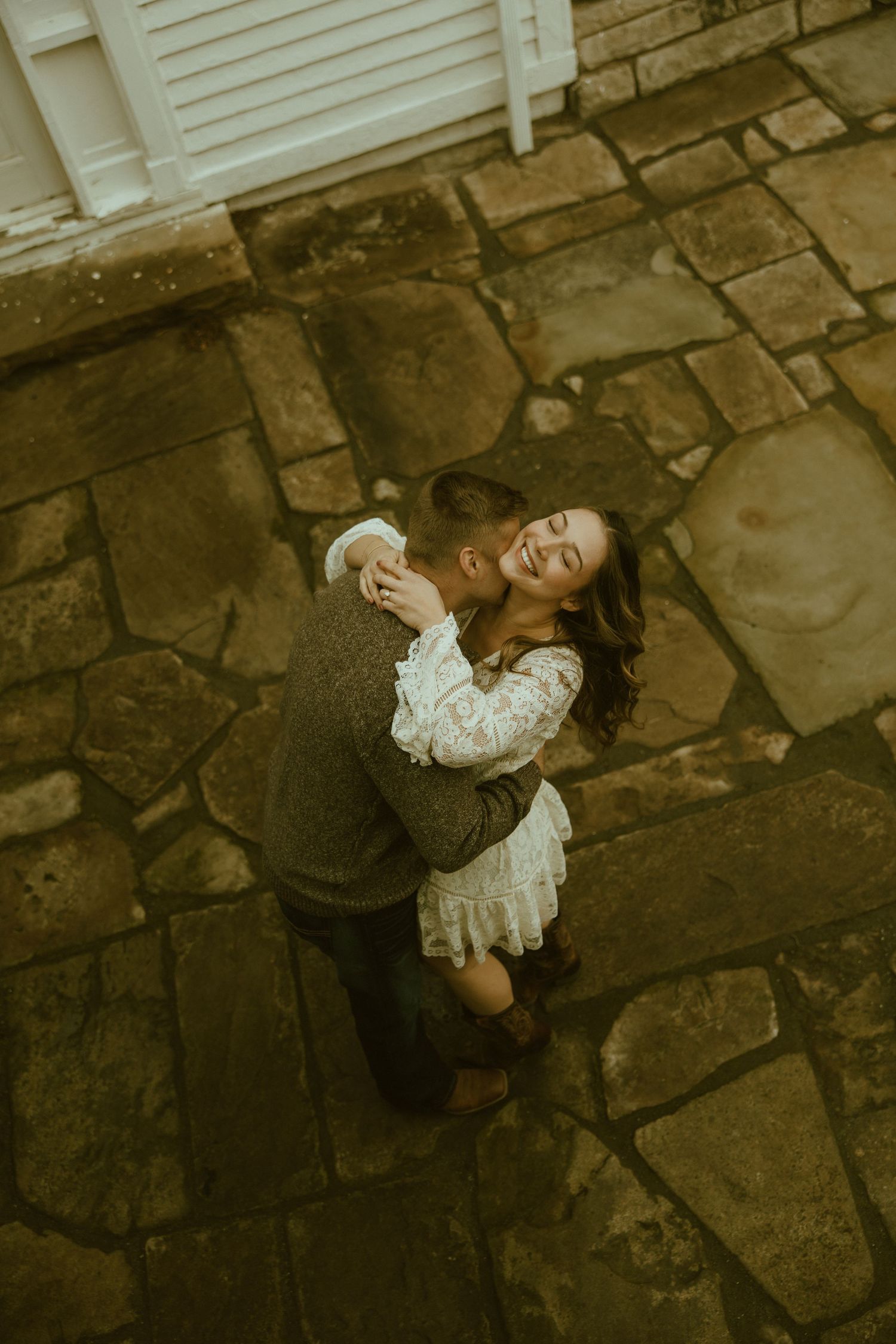 A couple dances intimately on vintage stone pavement, with the person in white wearing a flowing lace dress.