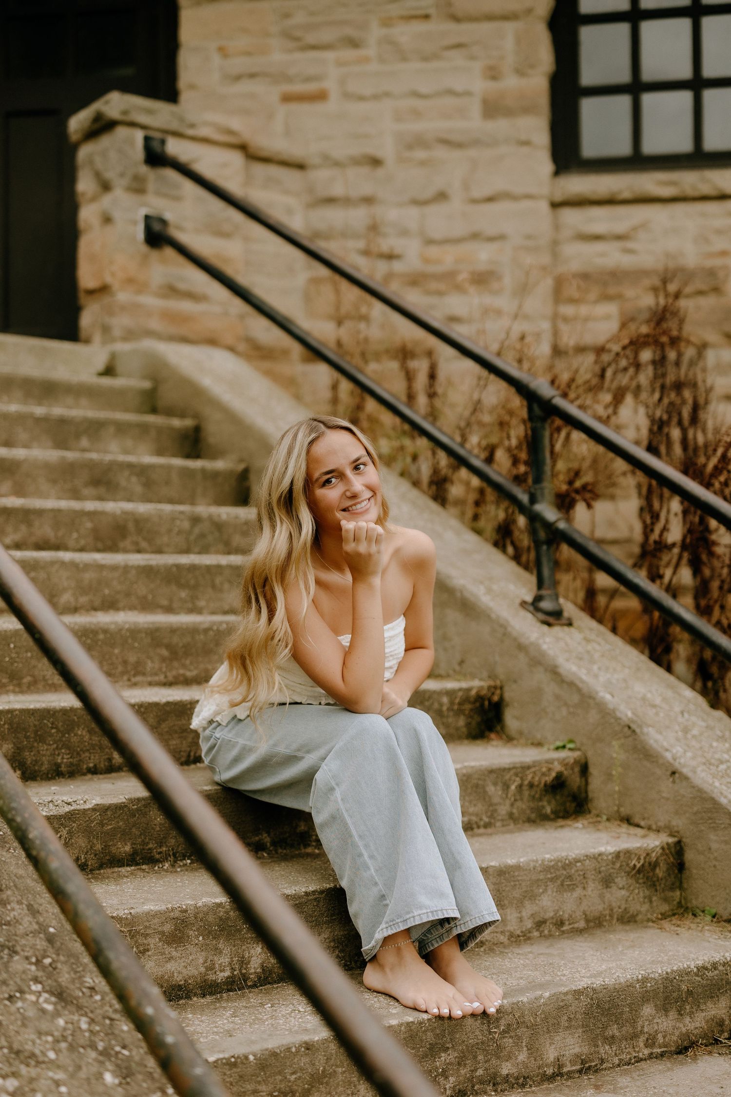 Casual portrait on stone steps with natural barefoot styling creates relaxed outdoor ambiance.