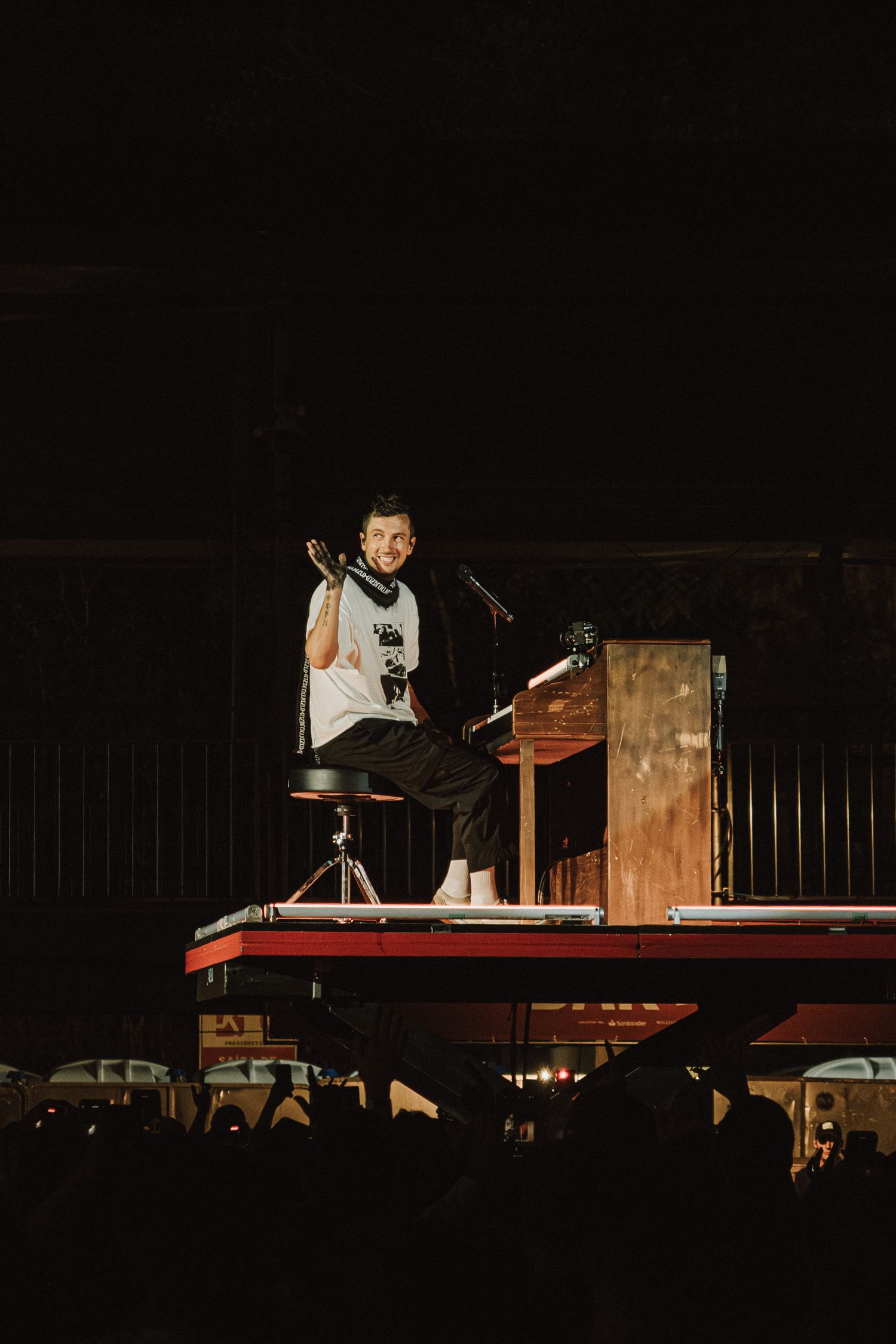 Musician performs at piano on elevated platform during nighttime concert.