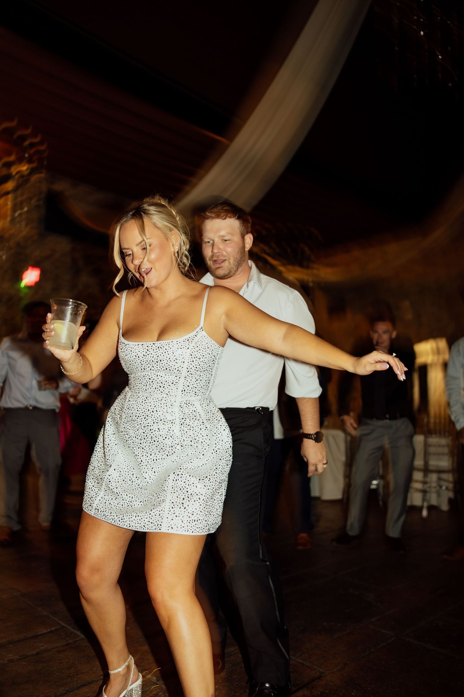 Wedding guests dancing energetically on a dimly lit dance floor during evening reception celebrations.