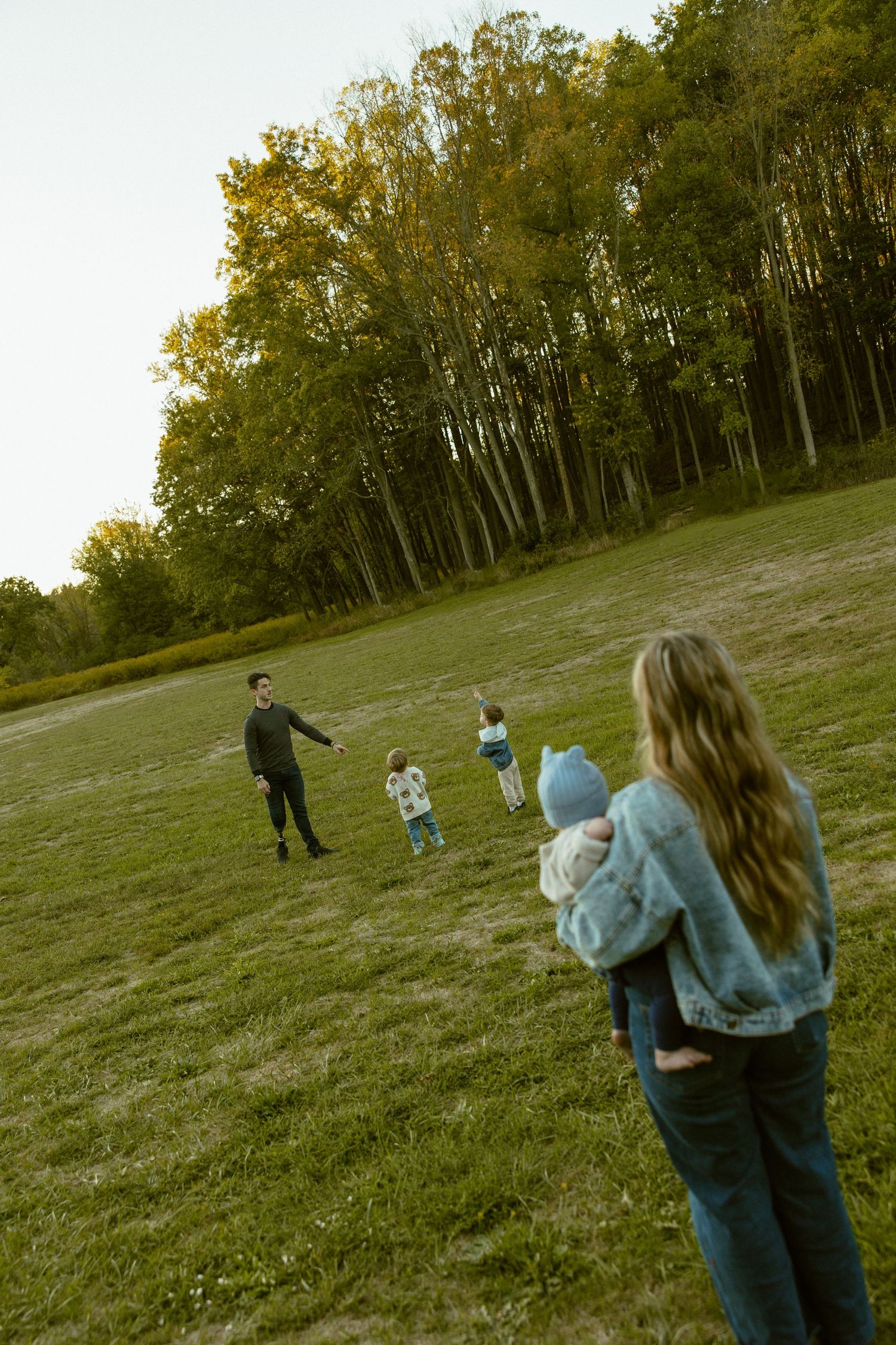 Two people play catch with a ball in a grassy field surrounded by autumn trees at sunset.