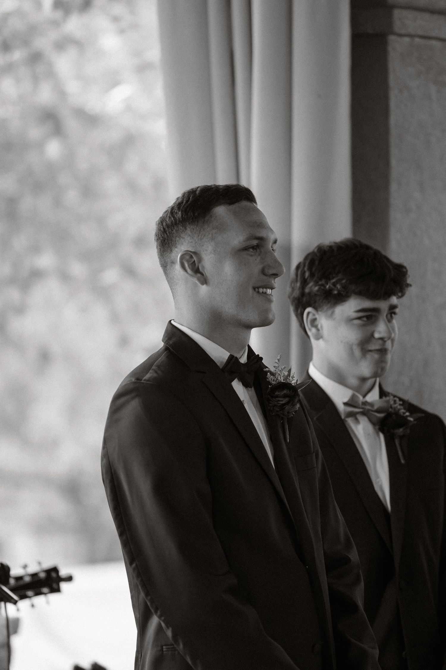 Candid black and white photo of groomsmen sharing a laugh indoors.