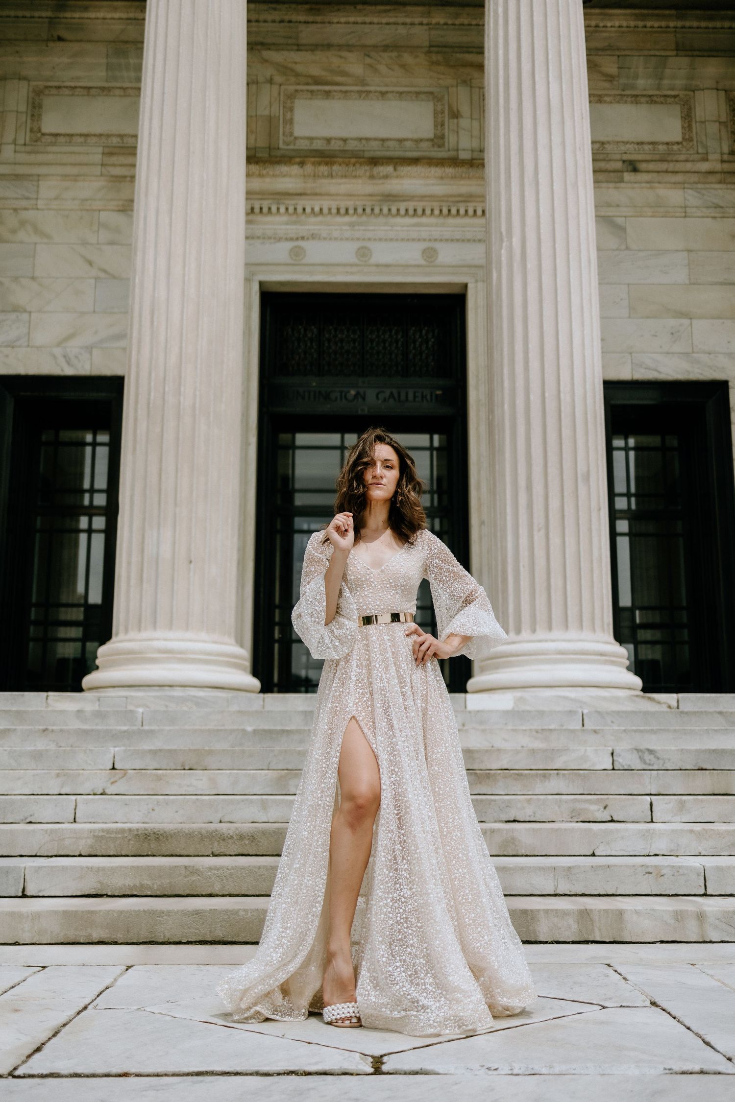 An elegant bridal pose showcases a stunning lace gown against neoclassical architecture.