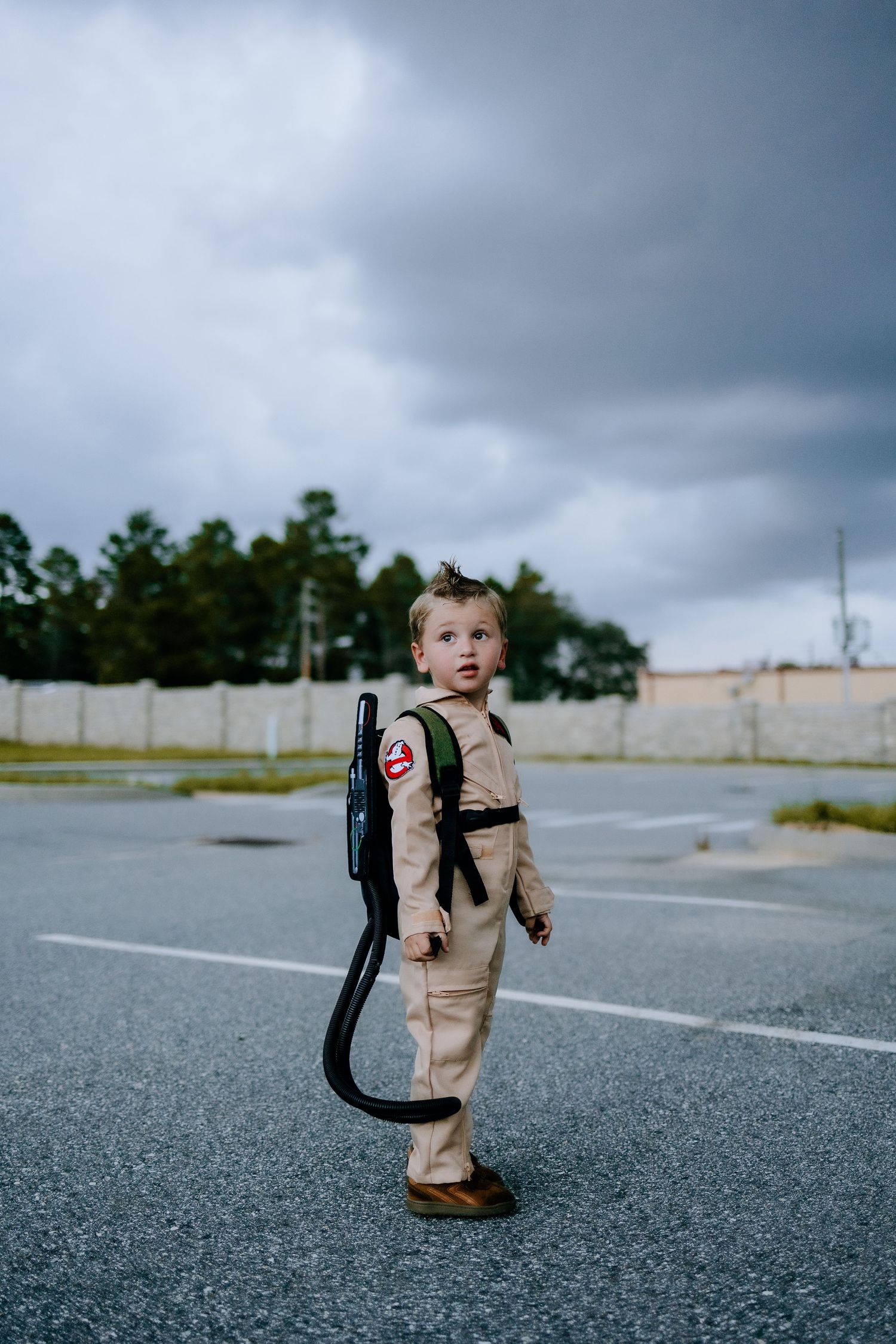 A miniature ghostbuster stands ready with proton pack in a misty parking area.