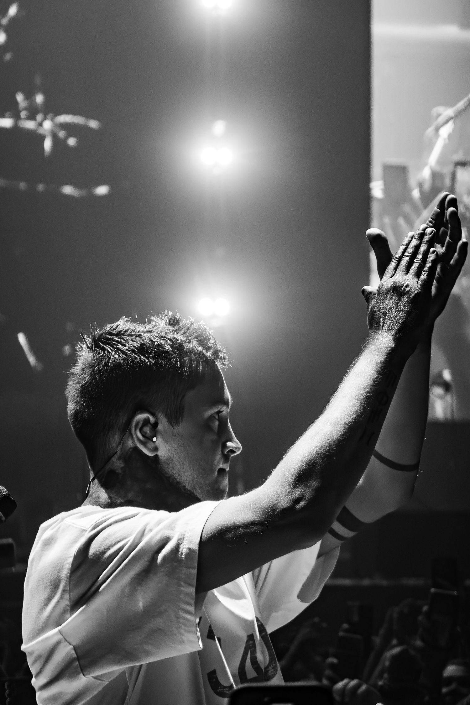 Concert performer raises hands in worship-like pose under dramatic stage lighting.