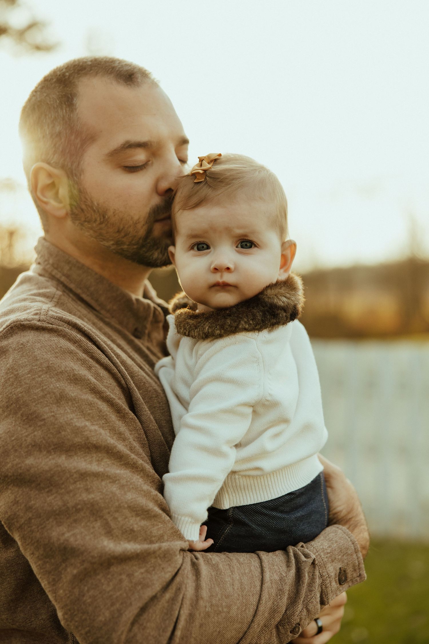 A tender moment captured in warm light as an adult embraces a baby wearing a white sweater outdoors.
