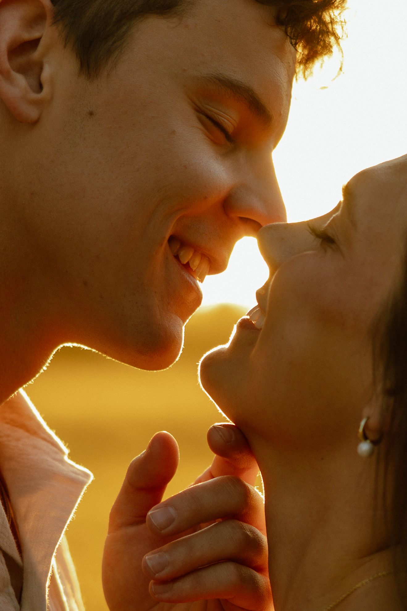 A romantic silhouette of a couple about to kiss in warm golden sunlight at sunset.