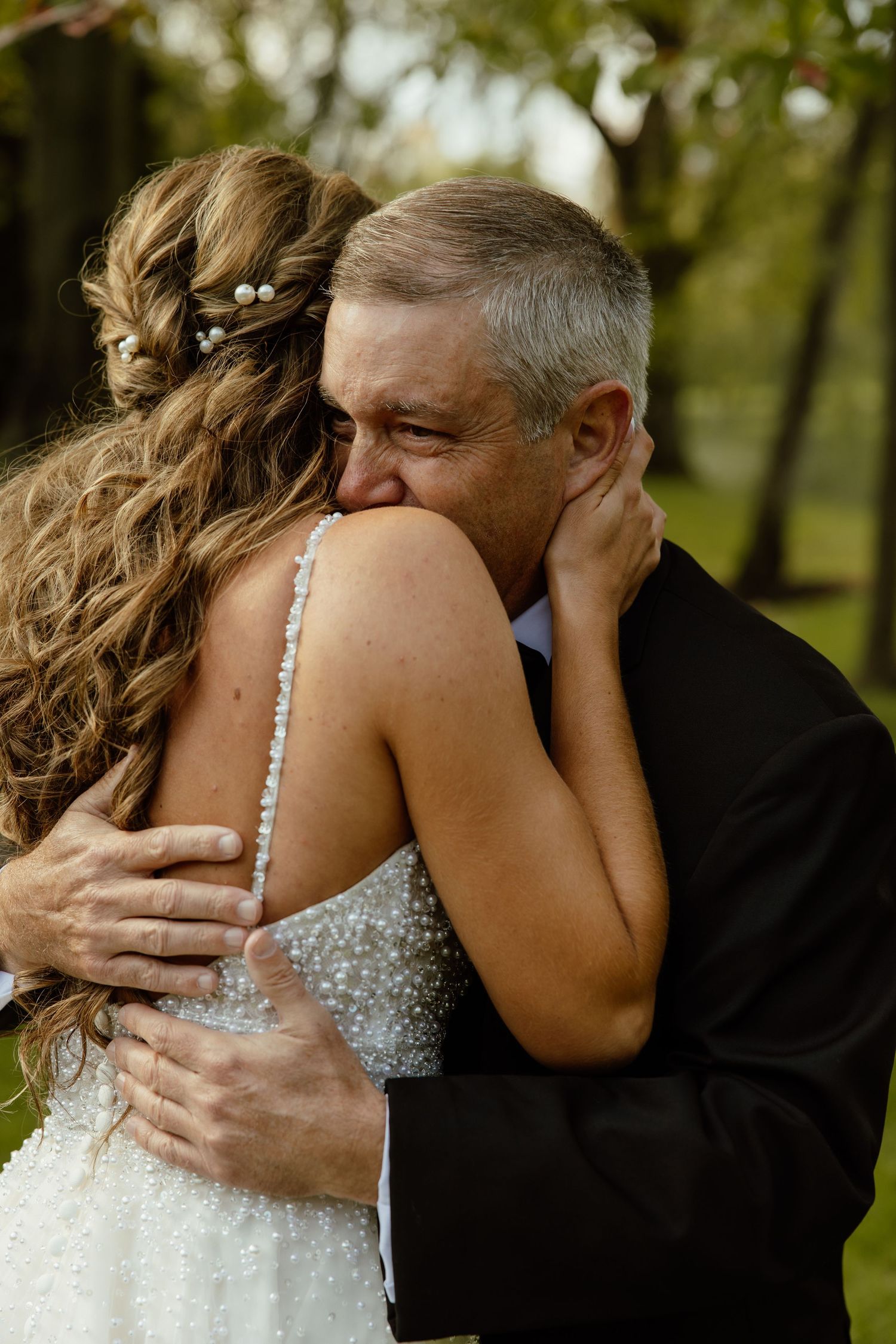 An emotional embrace between a bride in a sparkly dress and someone in formal attire during a wedding.