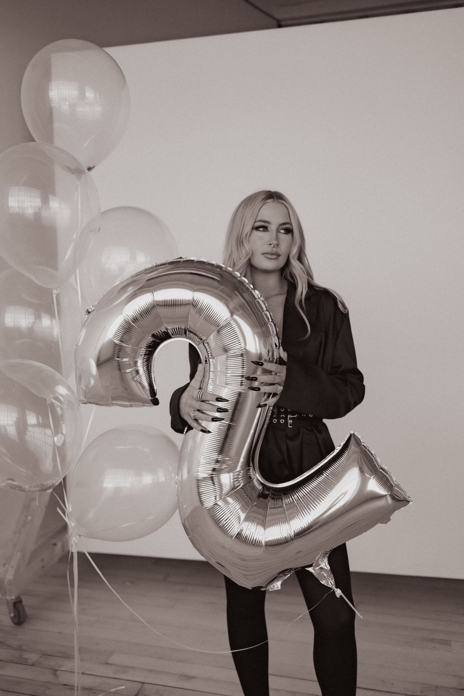 Person in black outfit poses with silver number balloon and white balloon display.