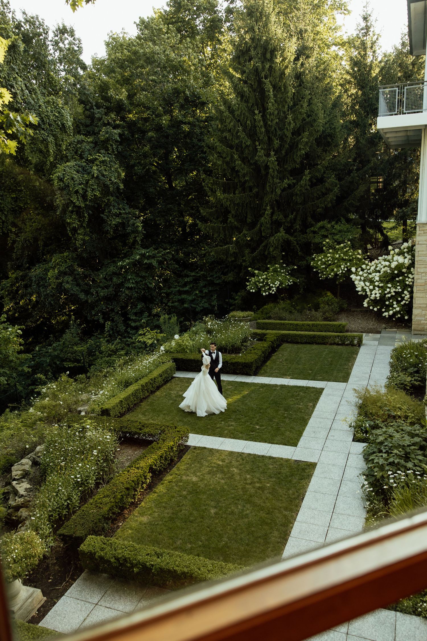 Aerial view of a wedding couple in a formal garden with geometric hedges and white stone pathways.