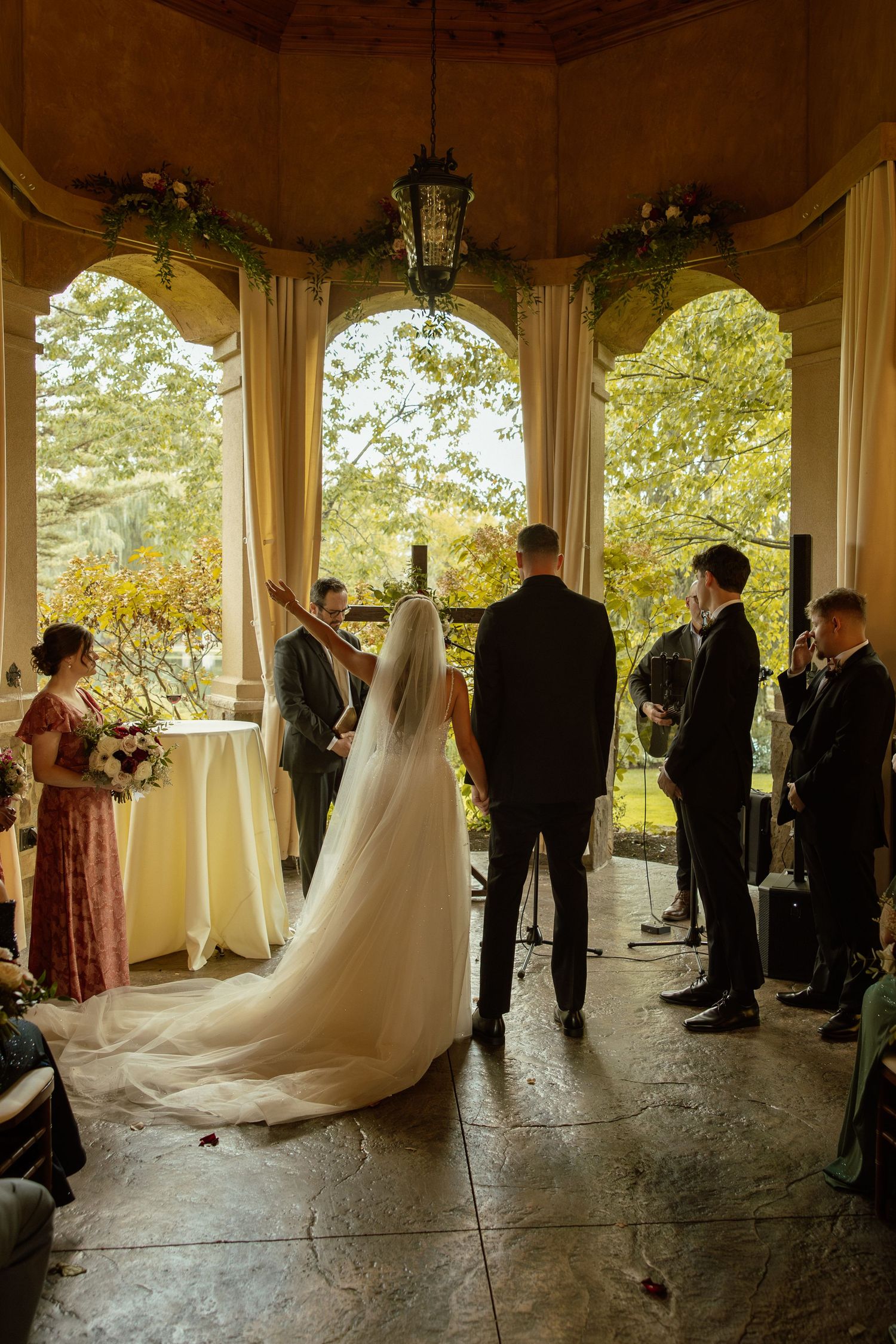 Wedding ceremony takes place under an elegant covered pavilion with stone flooring.