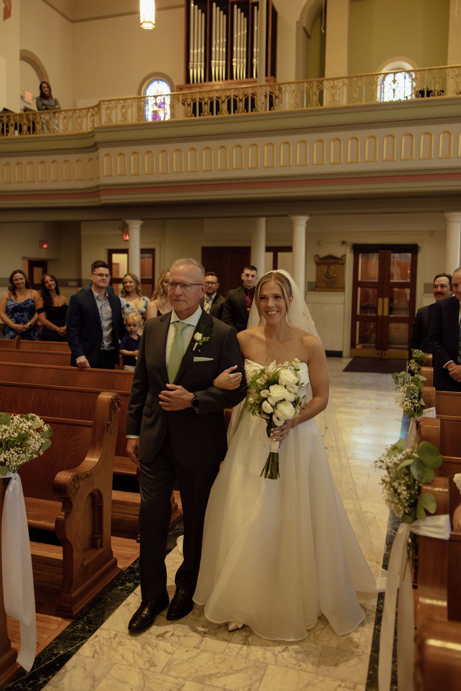 A wedding ceremony in a traditional church with ornate architecture featuring an organ loft and stained glass windows.