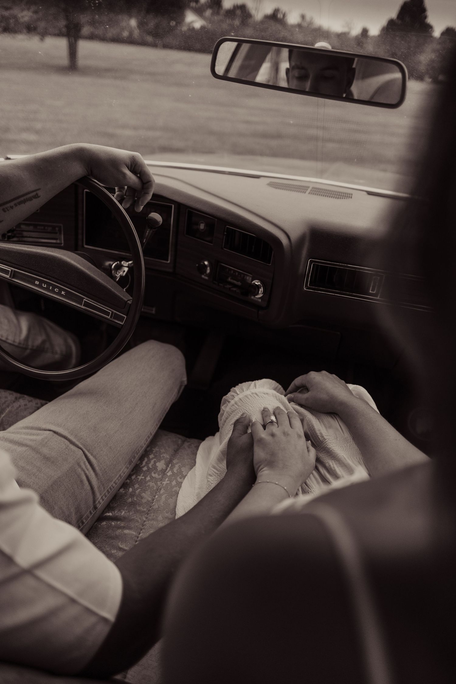 Black and white photo of a car interior with a rearview mirror and dashboard visible.