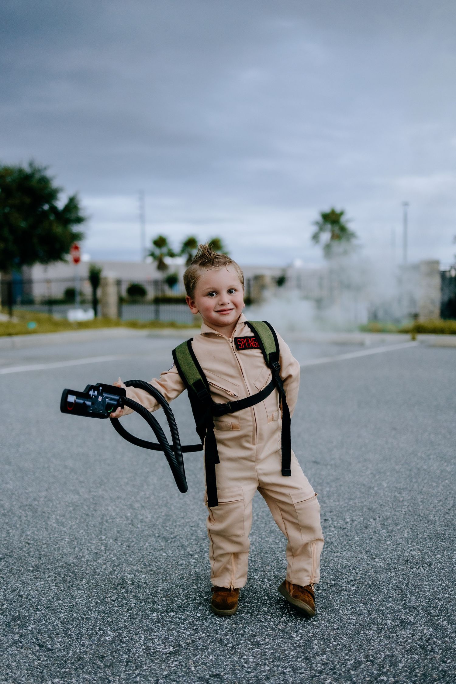 A tiny ghostbuster costume brings whimsy to an empty parking lot under stormy skies.