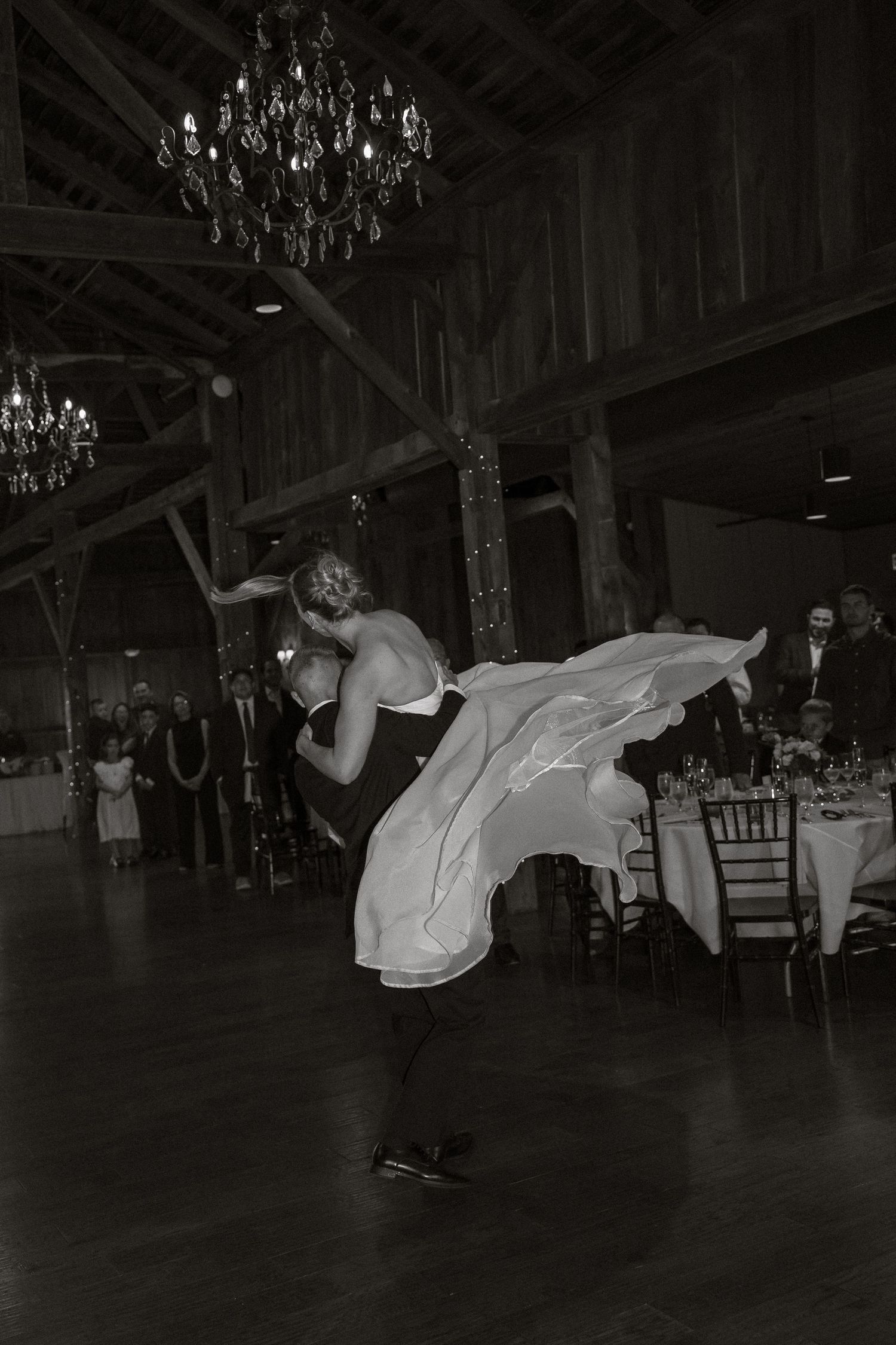 Black and white photos of wedding guests dancing and celebrating in a rustic barn venue with chandeliers.