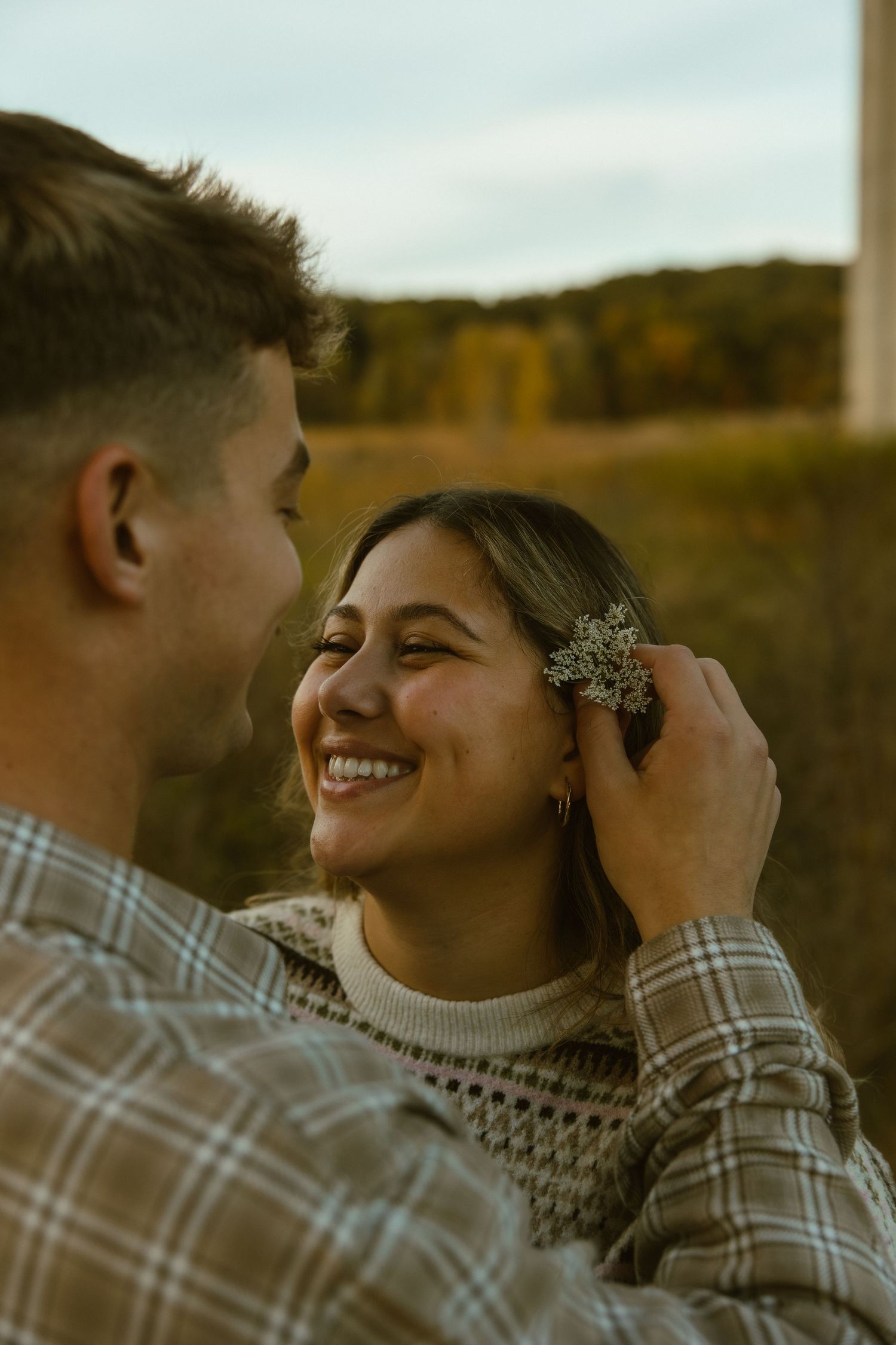 A couple shares an intimate moment outdoors during golden hour, with warm autumn colors in the background.