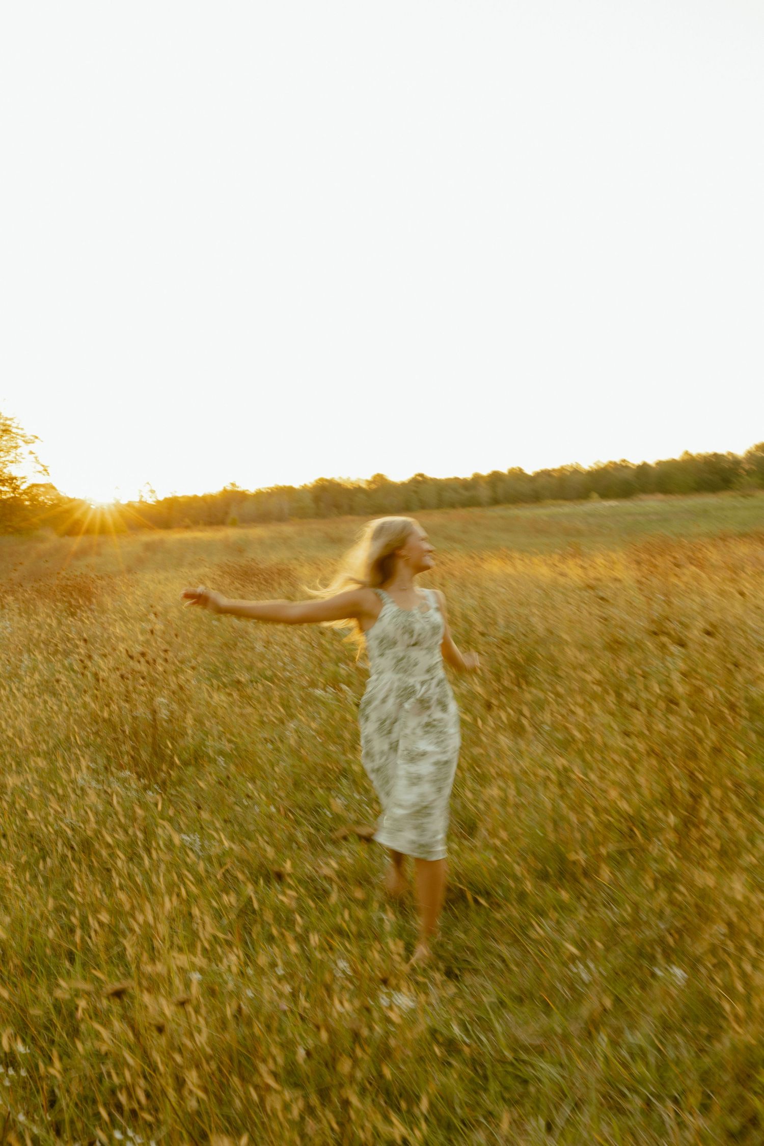 A person in a flowy dress spins joyfully through a golden sunlit field at sunset.
