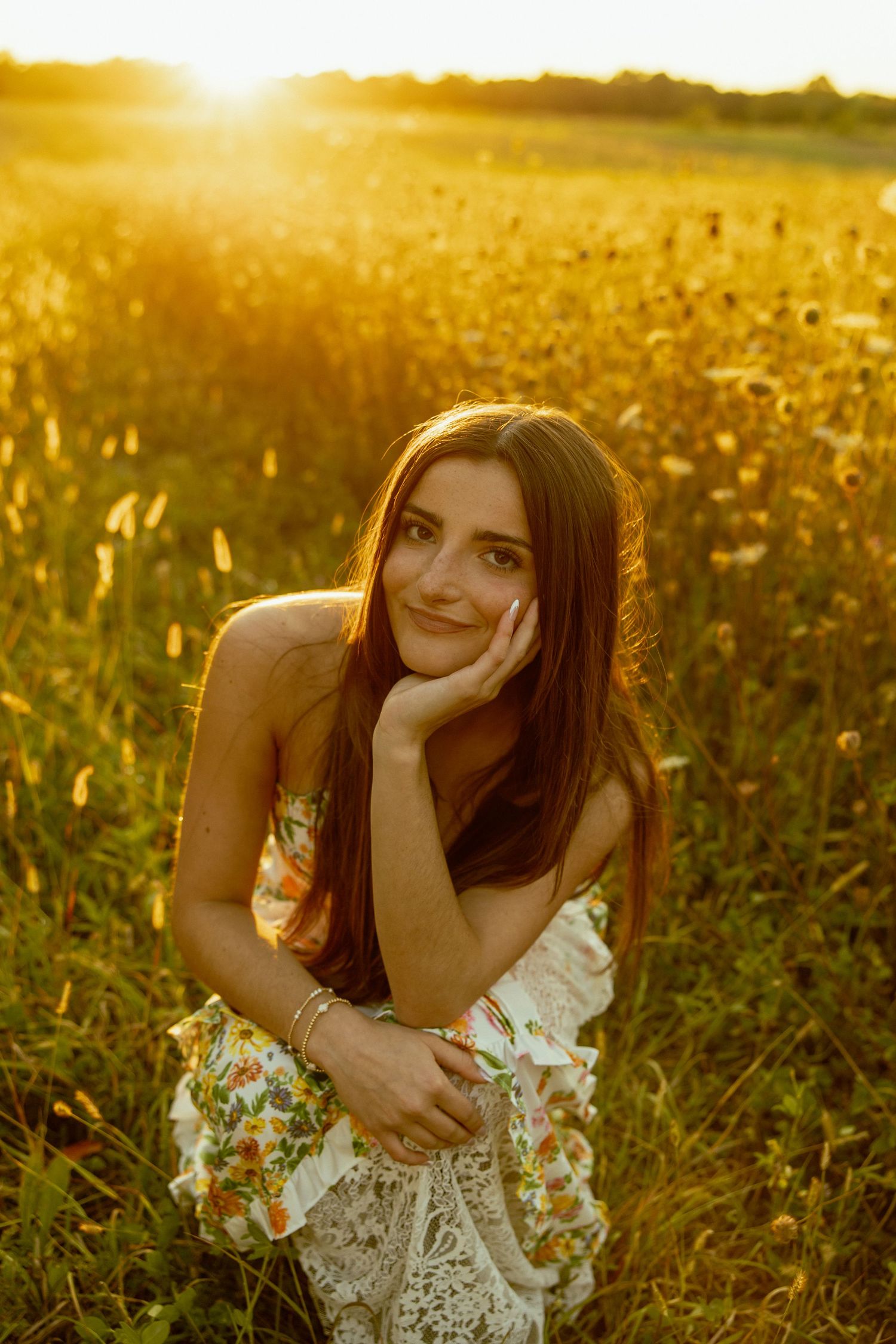 Person in floral dress sits dreamily in sunlit field of tall golden wheat during sunset.