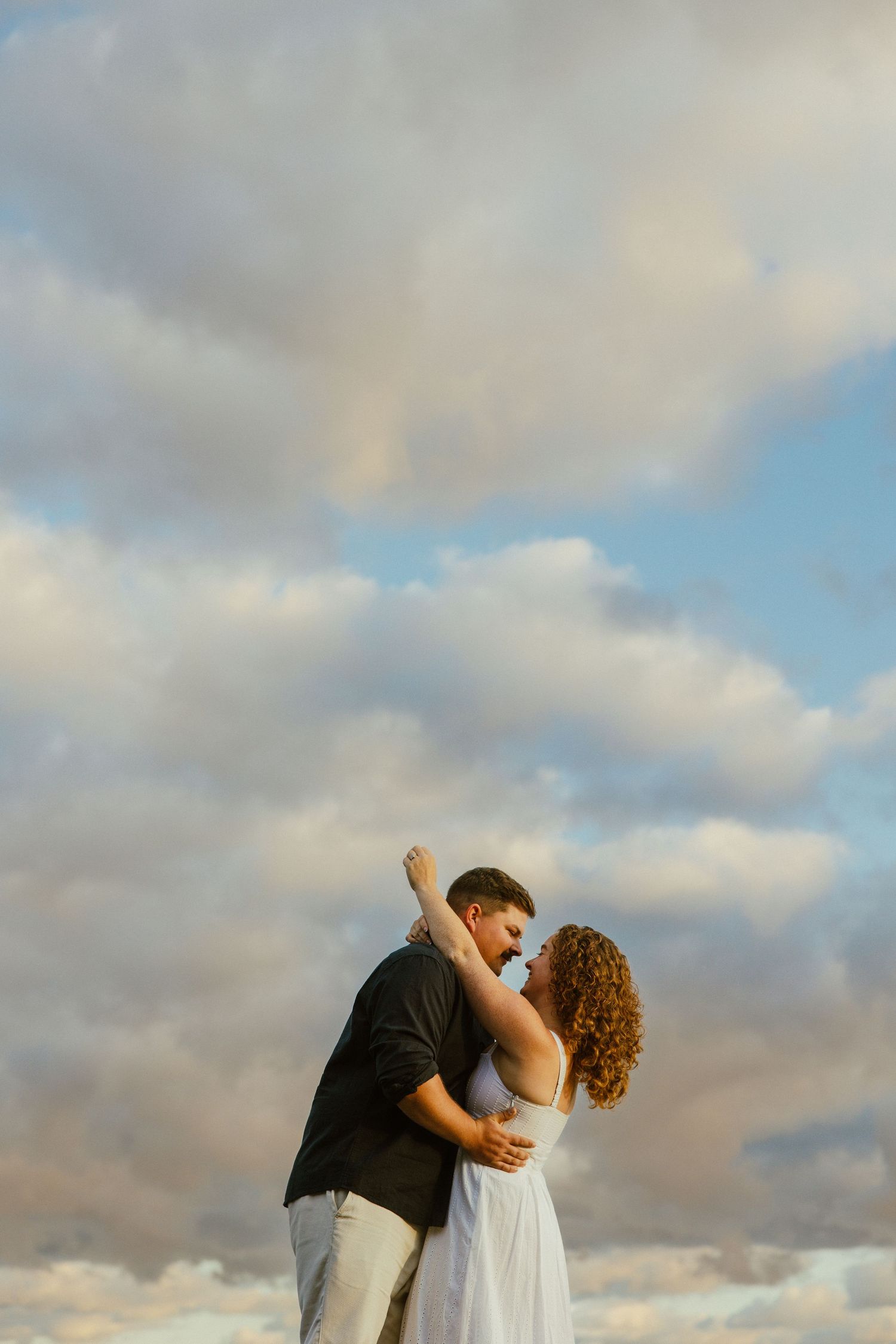 A couple dances together against a cloudy sky backdrop during golden hour.