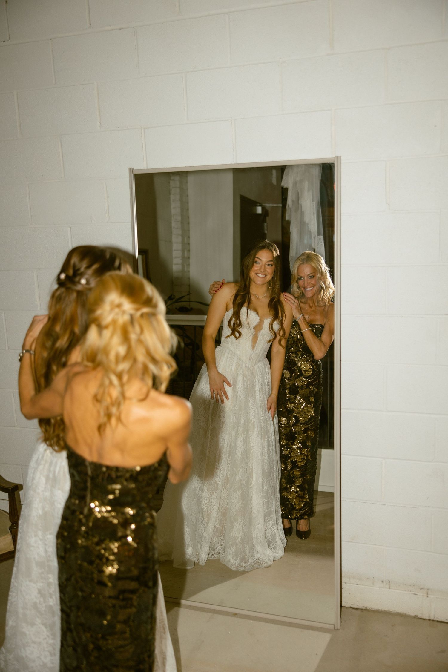 People in formal attire share joyful moments while taking photos in front of a white wall at an event.