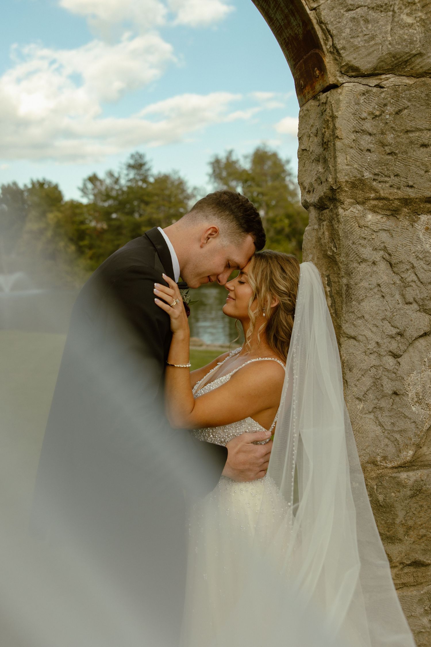 An intimate wedding moment captured beneath a rustic stone archway on a sunny afternoon.