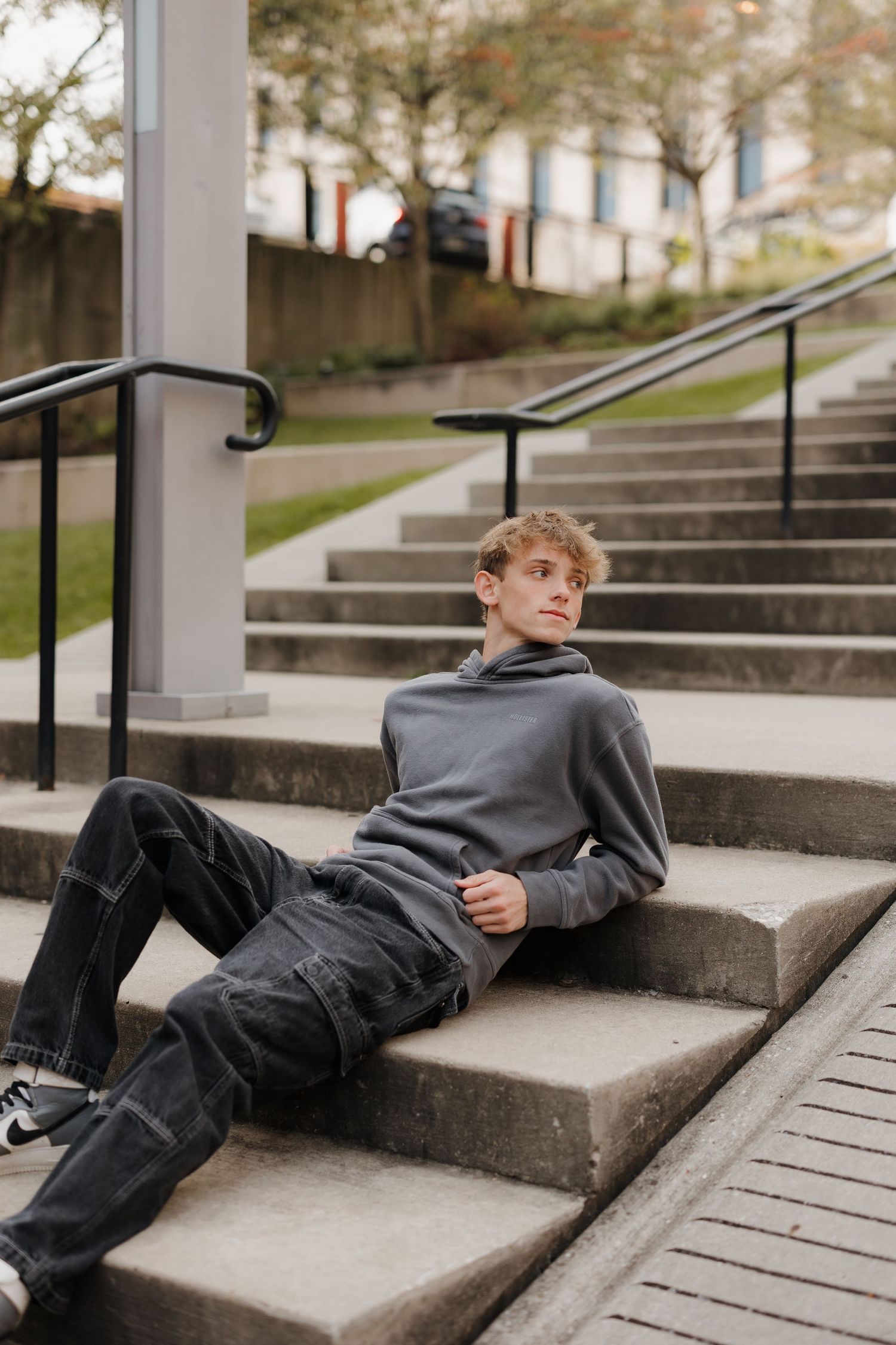 Urban portrait of someone lounging on concrete steps wearing a grey sweater and dark jeans.