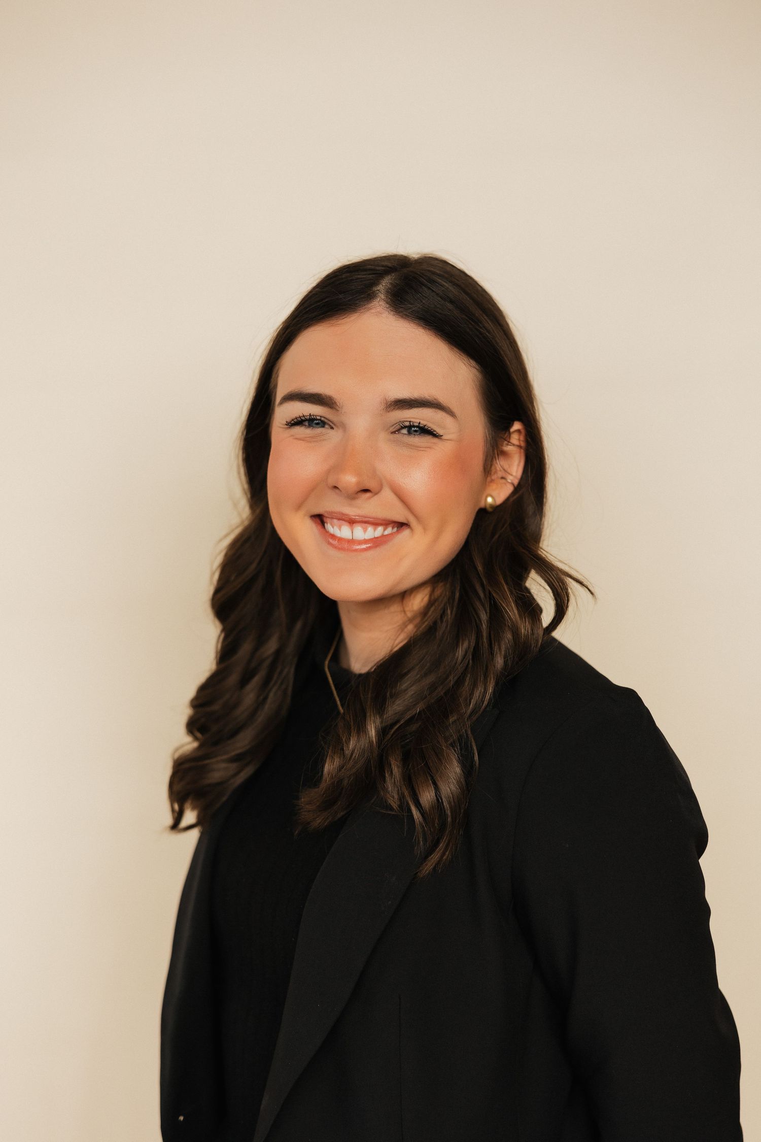 Professional headshot of person in black blazer against neutral background.