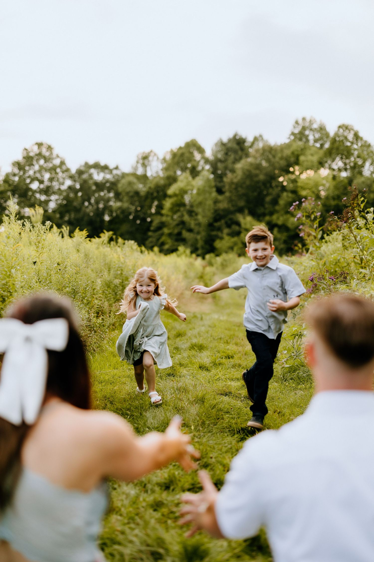Children running joyfully through a sunlit meadow towards their parents.