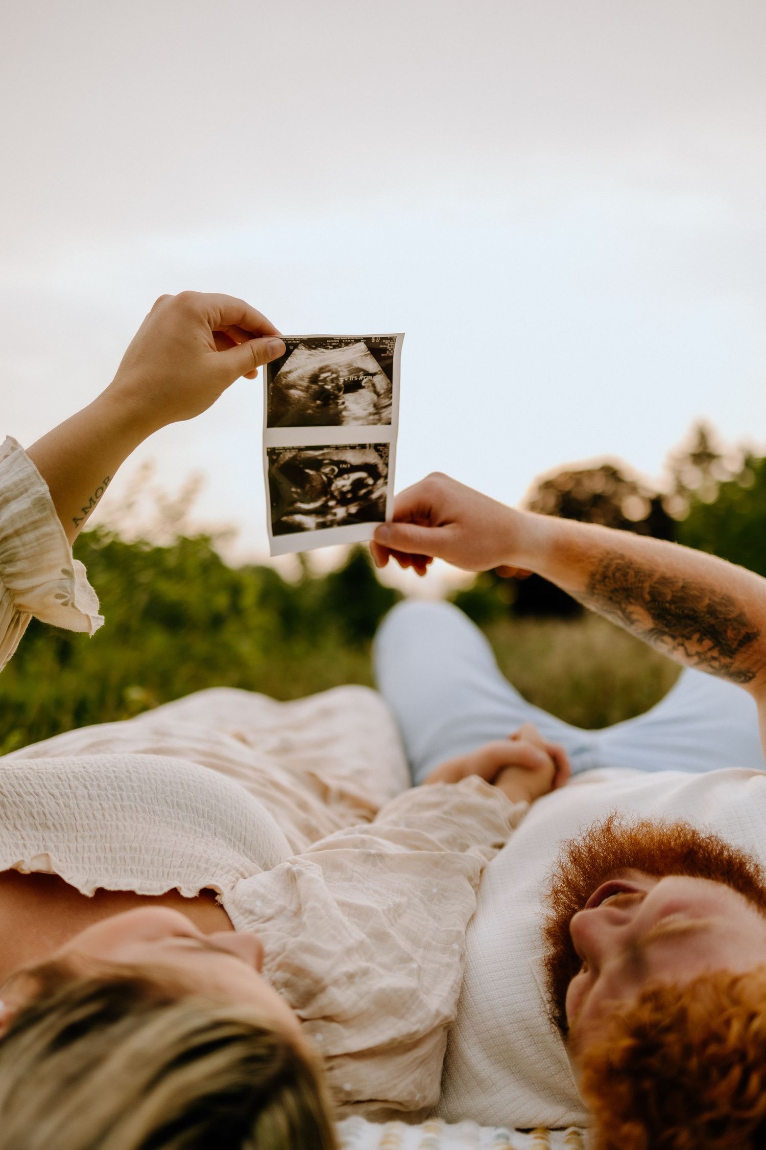 Couple lying down sharing ultrasound photos during a sunset outdoor photo session.
