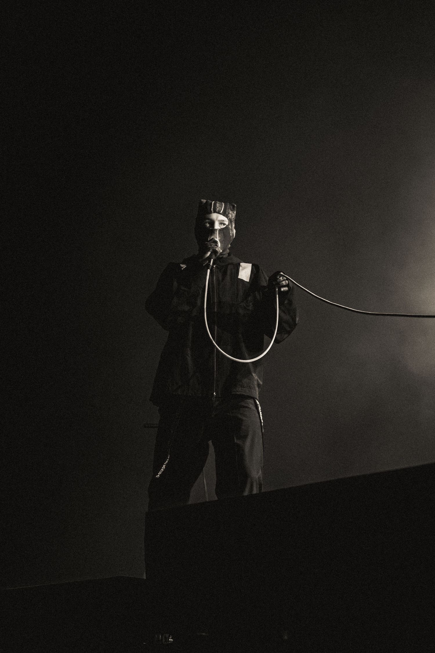 Black and white concert photo of performer on stage with microphone in dramatic lighting.