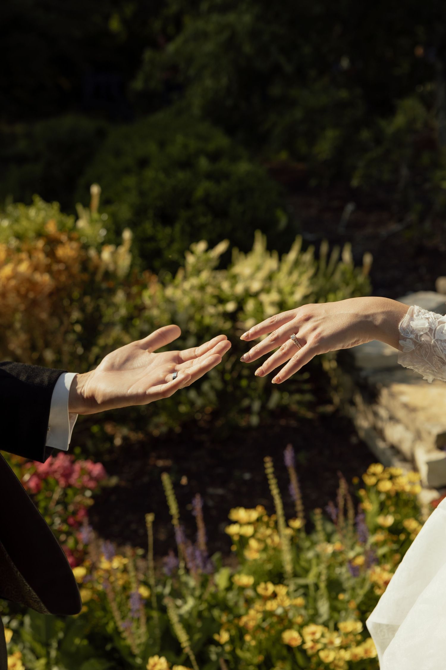 Hands reaching out against a sunlit garden backdrop during an outdoor wedding ceremony.