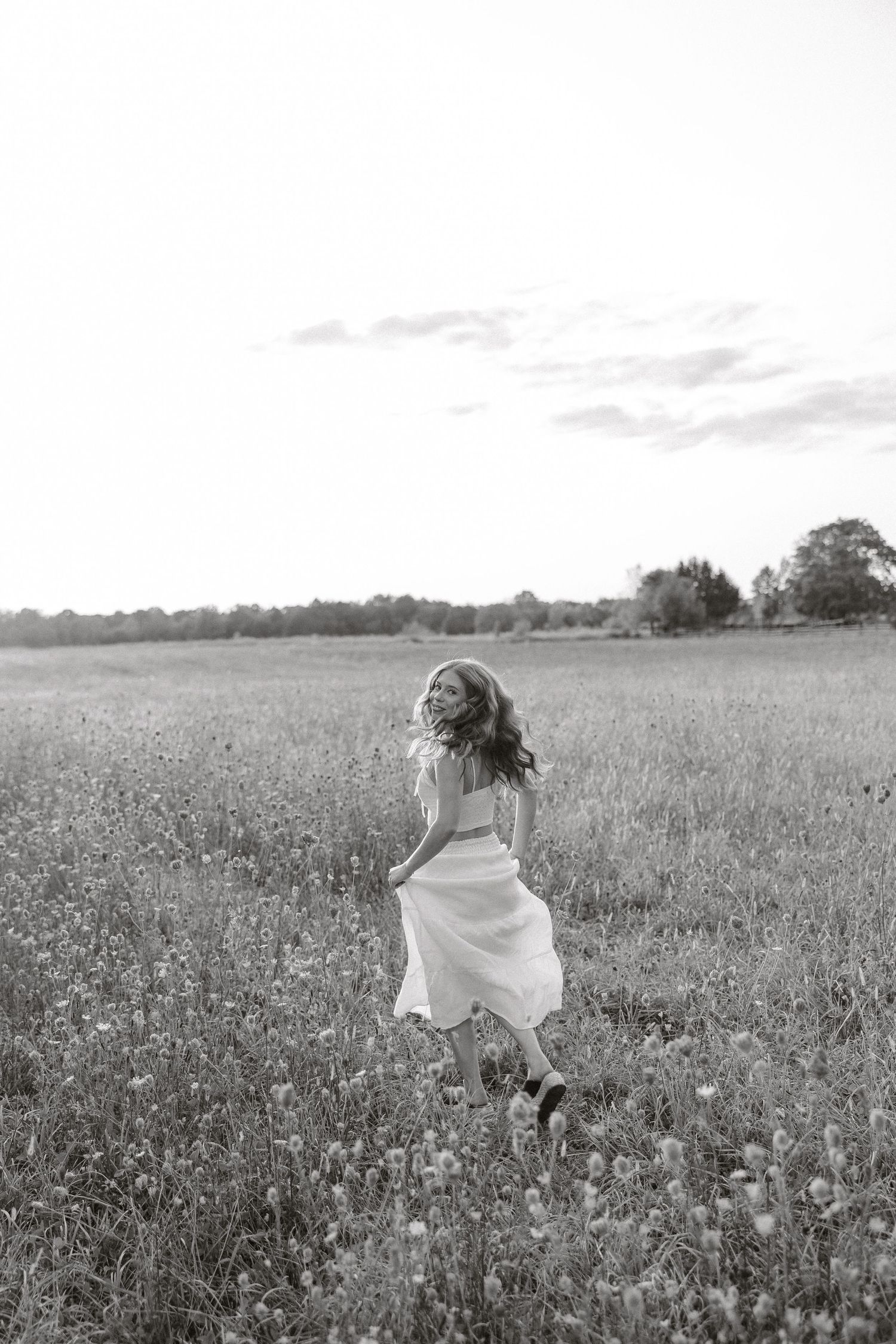 Black and white photo of someone dancing through a flowering meadow in a flowing white dress.