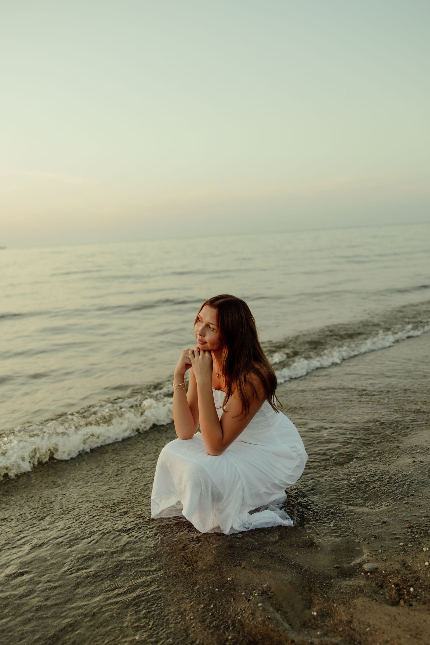 A person in a white dress reclines at the ocean's edge during sunset, creating a dreamy beachside scene.