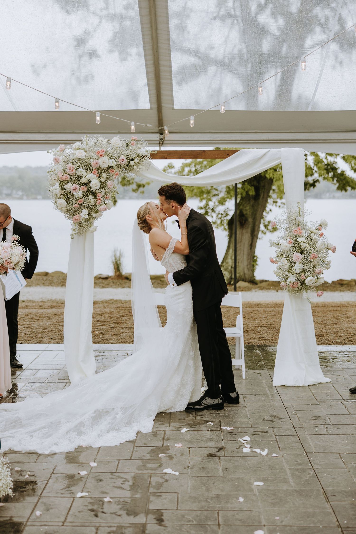 Wedding couple shares a romantic moment under a white tent decorated with flowing fabric and floral arrangements.