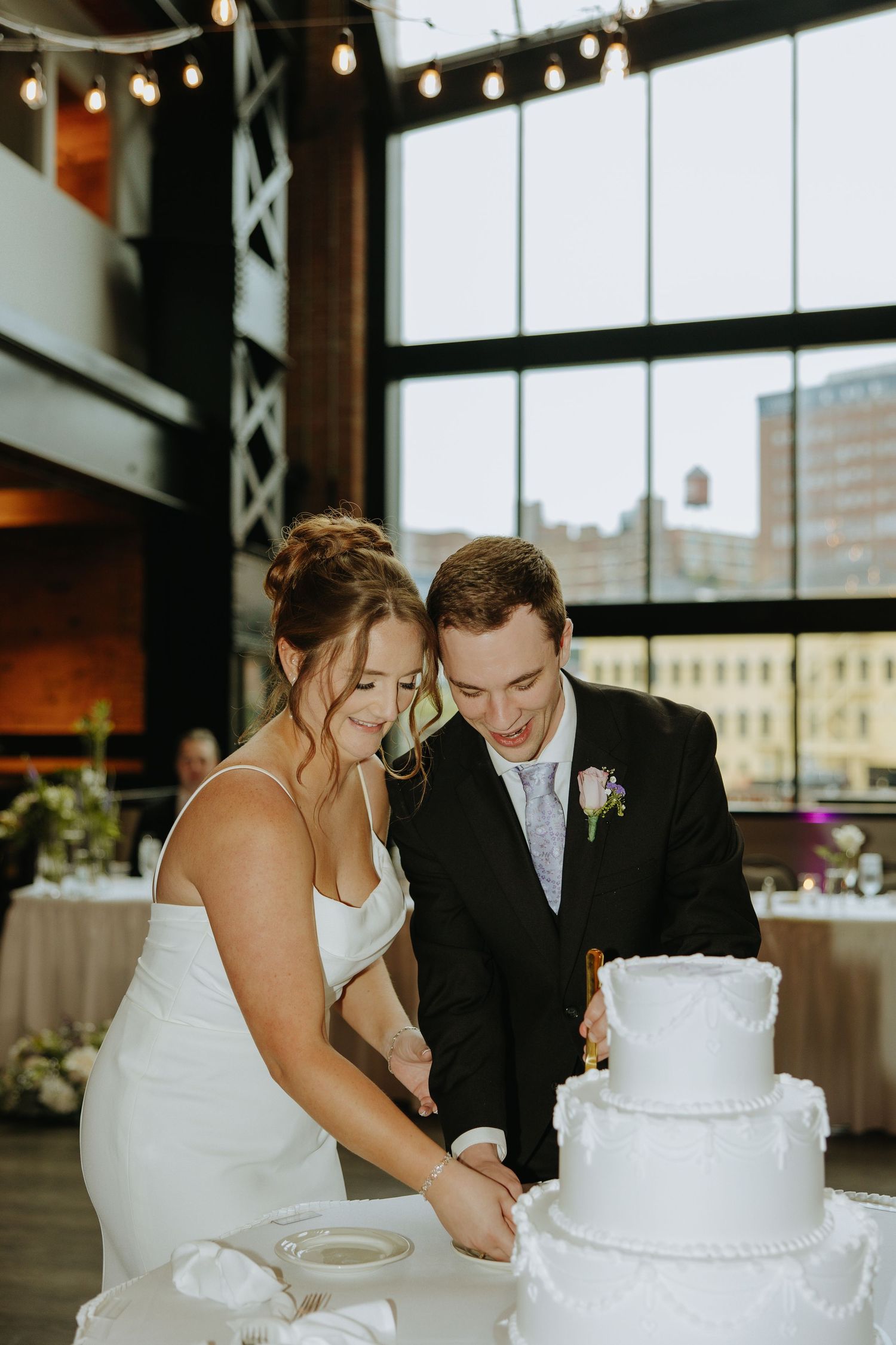 Wedding couple cuts their elegant white tiered cake together at reception.