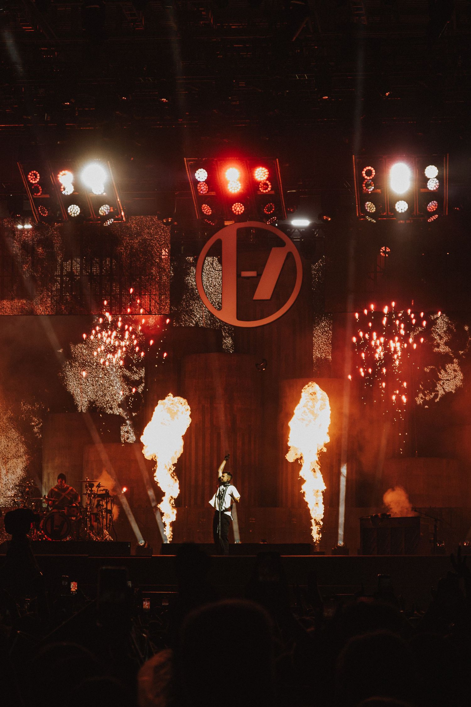 Concert stage with pyrotechnic flames and bright lighting effects displaying band logo.