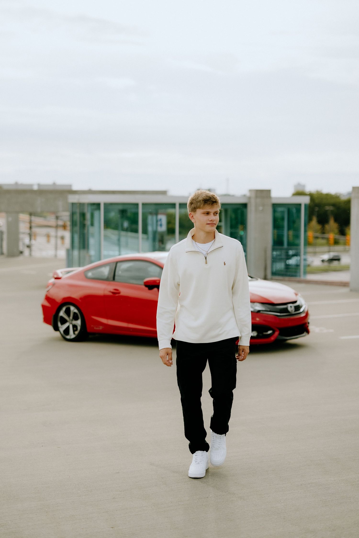Street fashion photo with red car and modern building backdrop.