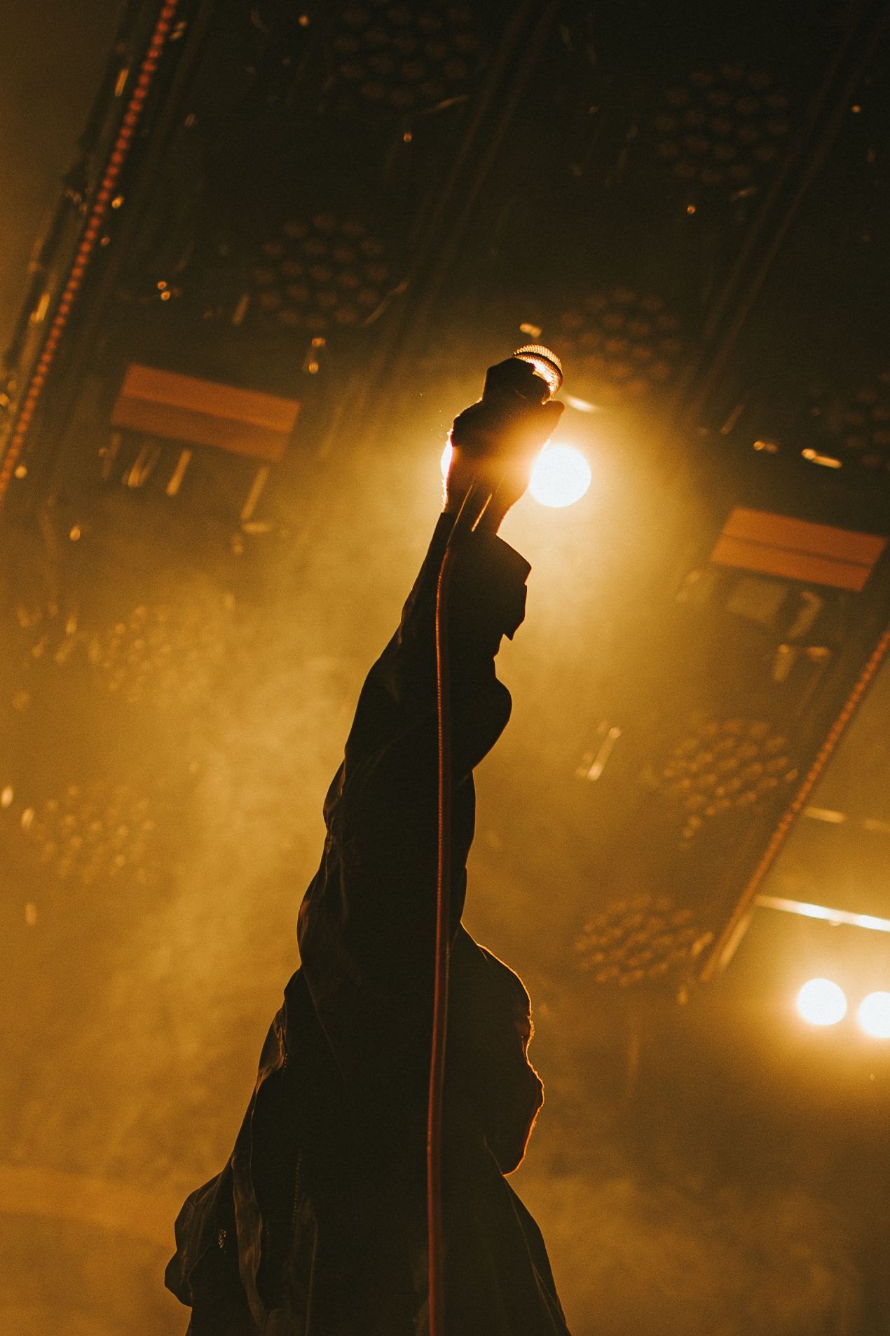 Silhouette of a performer on stage in dramatic backlighting with golden glow during concert performance.
